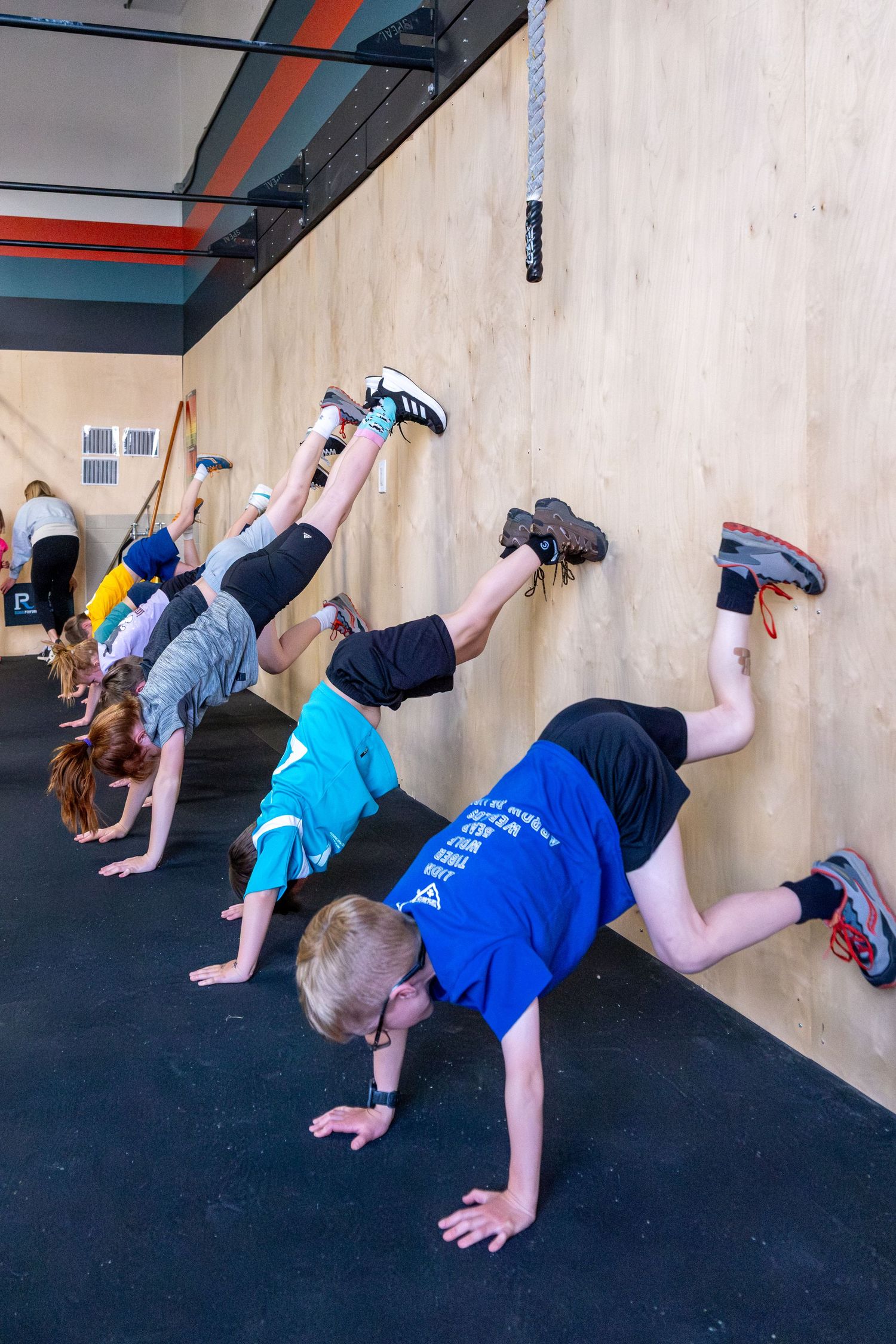 Children practice wall handstands during a CrossFit kids gymnastics class in a gym.