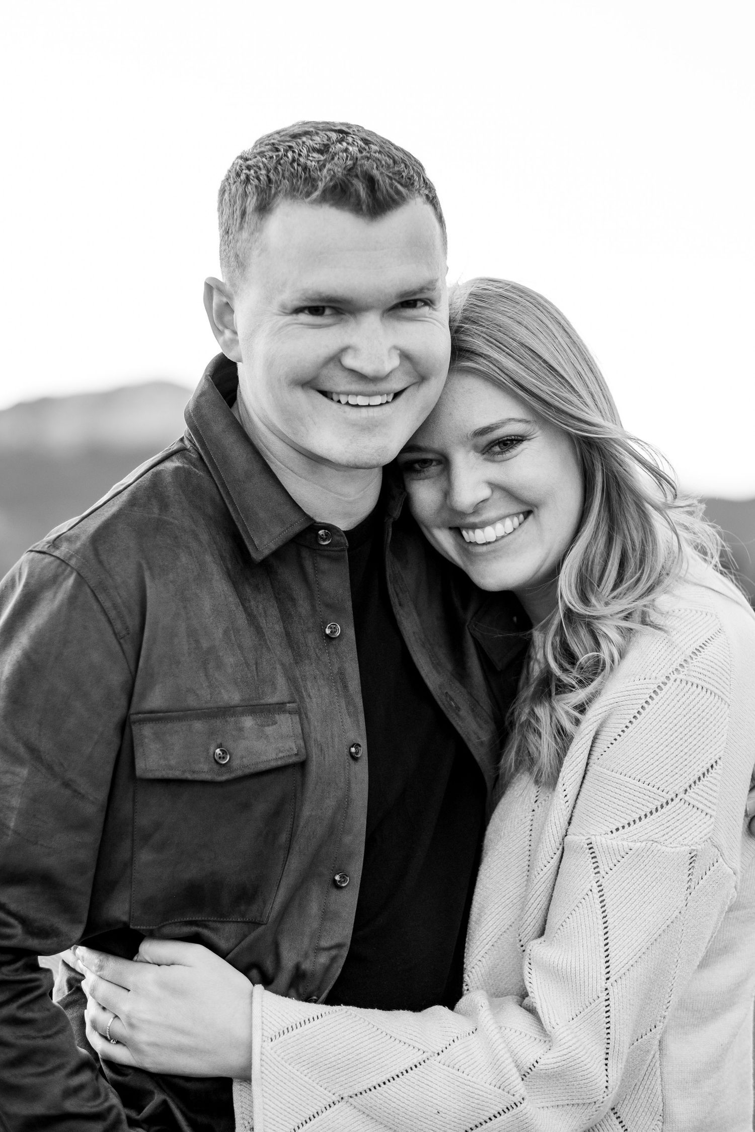Black and white portrait of smiling couple embracing closely during an outdoor photo session.