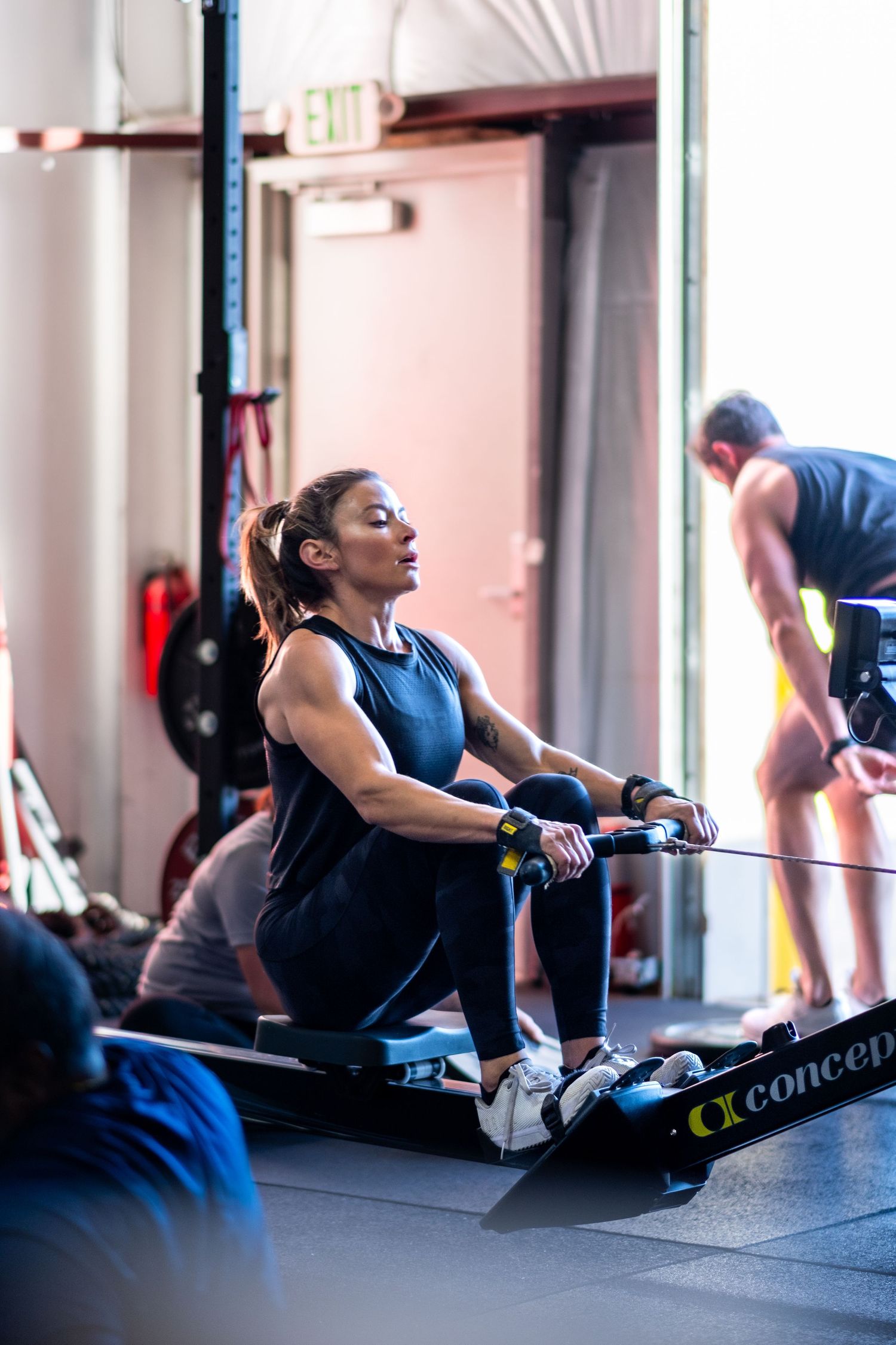 Woman using a Concept2 rowing machine during an intense gym workout session.