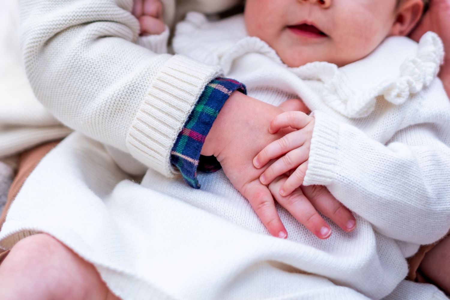 Tender close-up of a newborn baby holding an older childs hand wearing a colorful plaid bracelet.