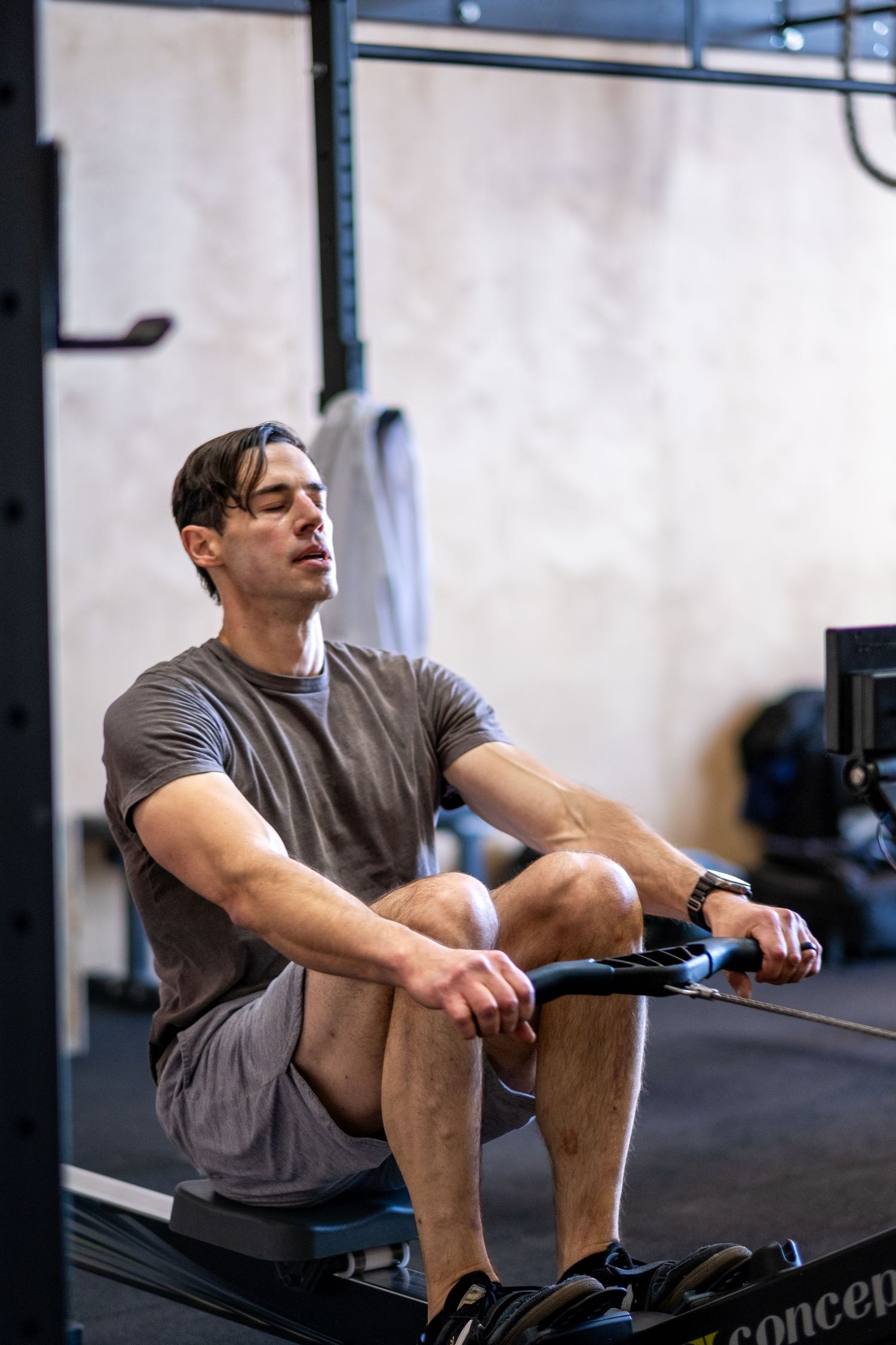 Focused male athlete rests between sets on a Concept2 rowing machine in a CrossFit gym.
