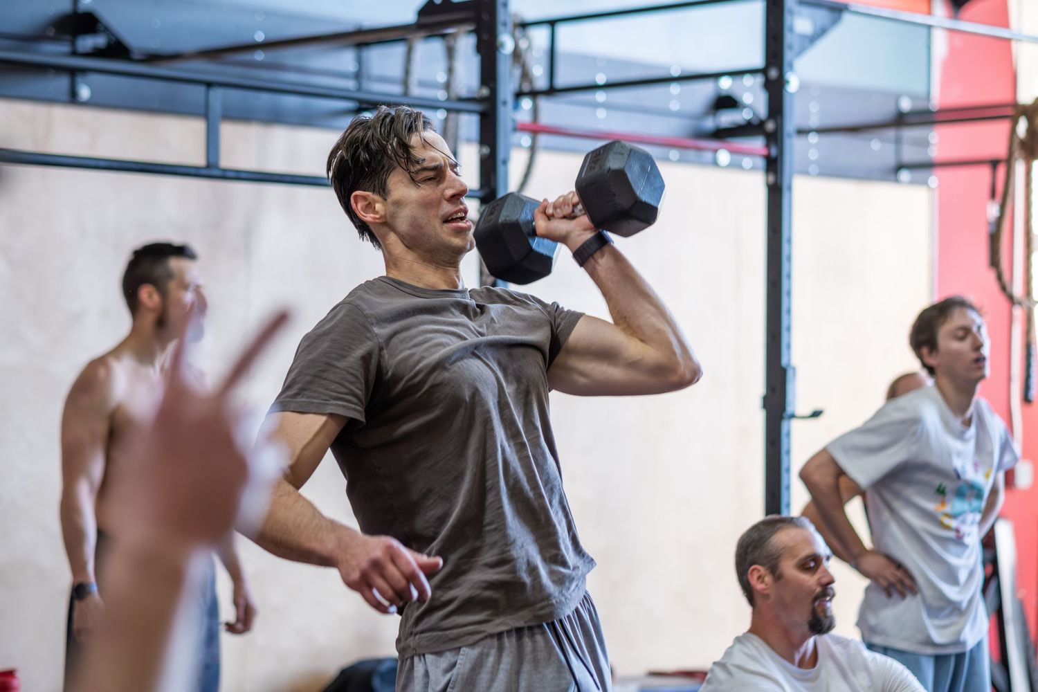 Athletic man performing a dumbbell overhead press exercise in a CrossFit gym.