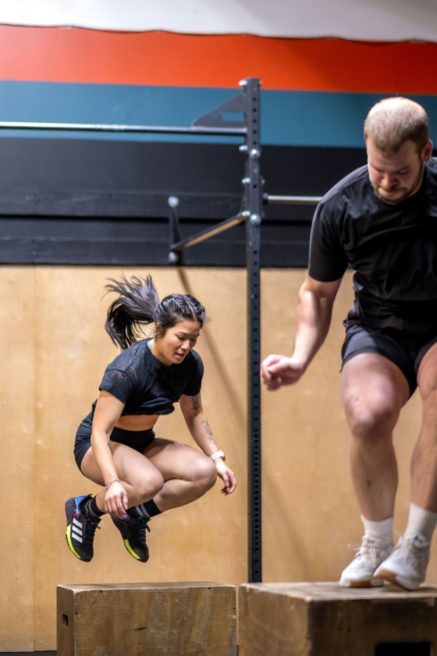 Man and woman performing synchronized box jumps during a CrossFit training session.