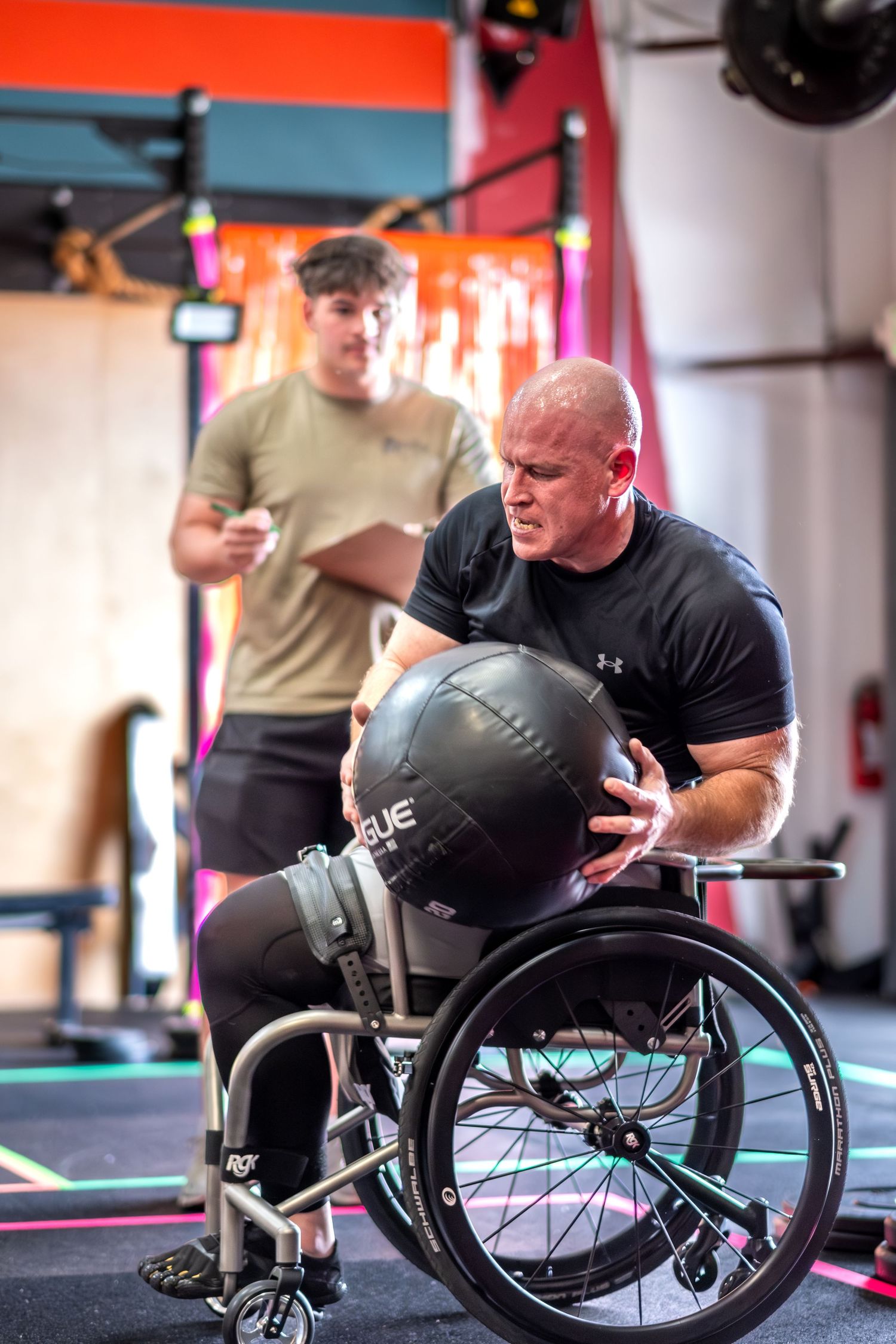 Muscular man in wheelchair performing medicine ball exercise at CrossFit gym.