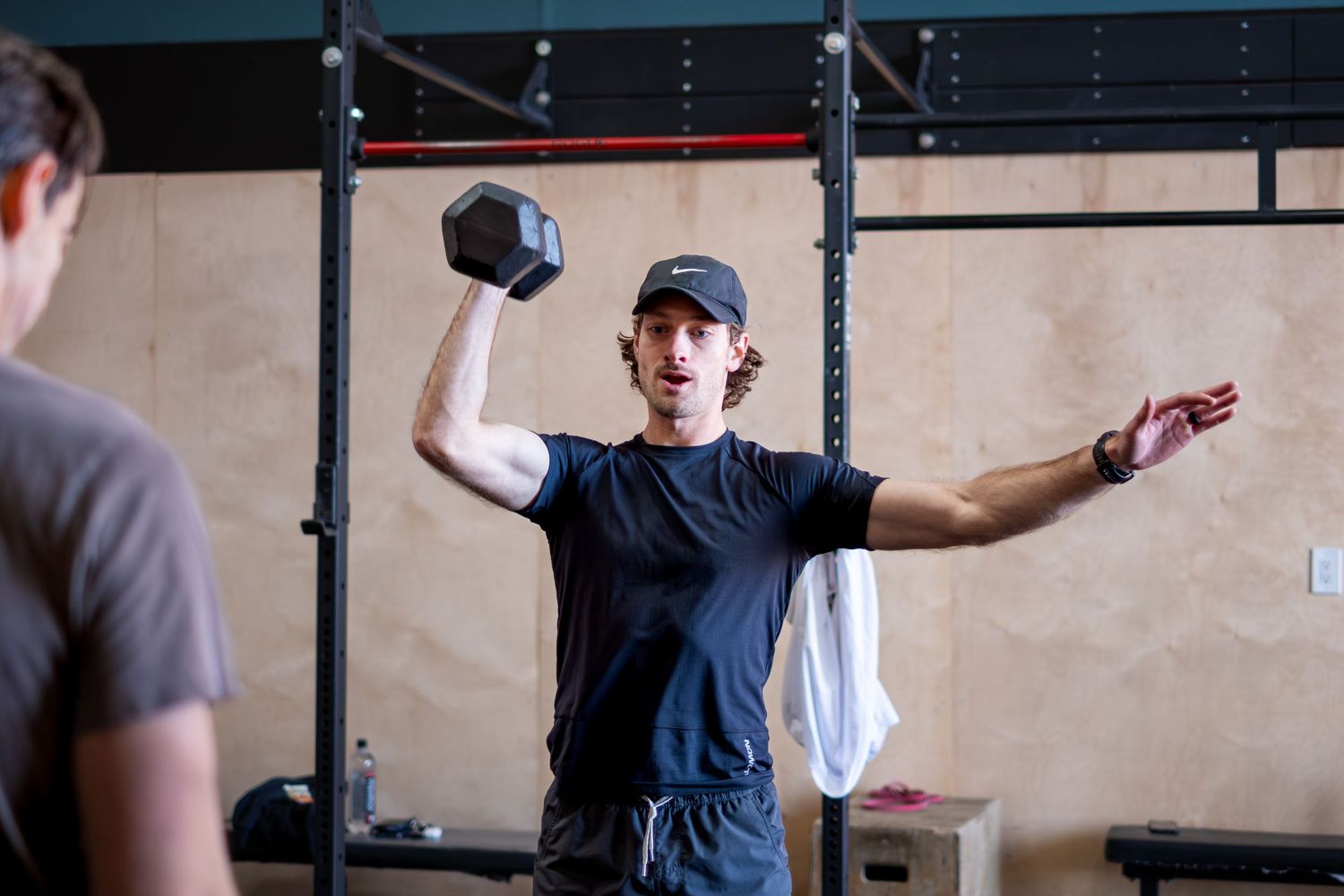 Man lifting a dumbbell overhead in a CrossFit gym during a workout session.