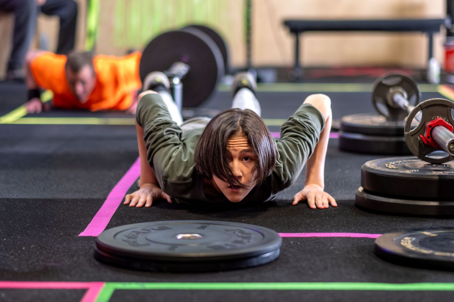 Woman doing push-ups on gym floor surrounded by barbell weight plates.