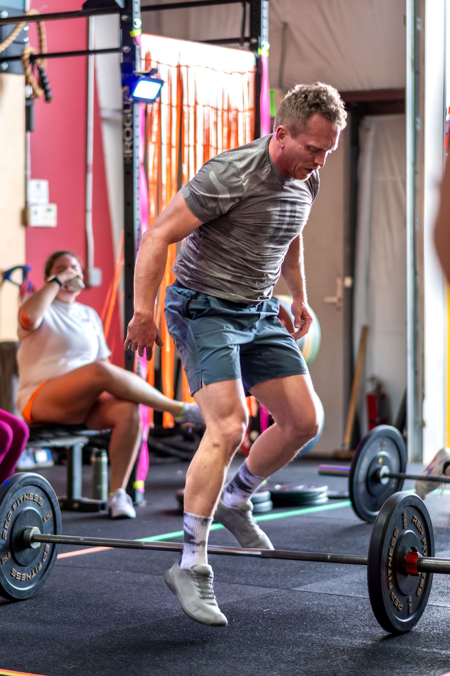 Athletic man jumping near loaded barbell during CrossFit workout in gym.