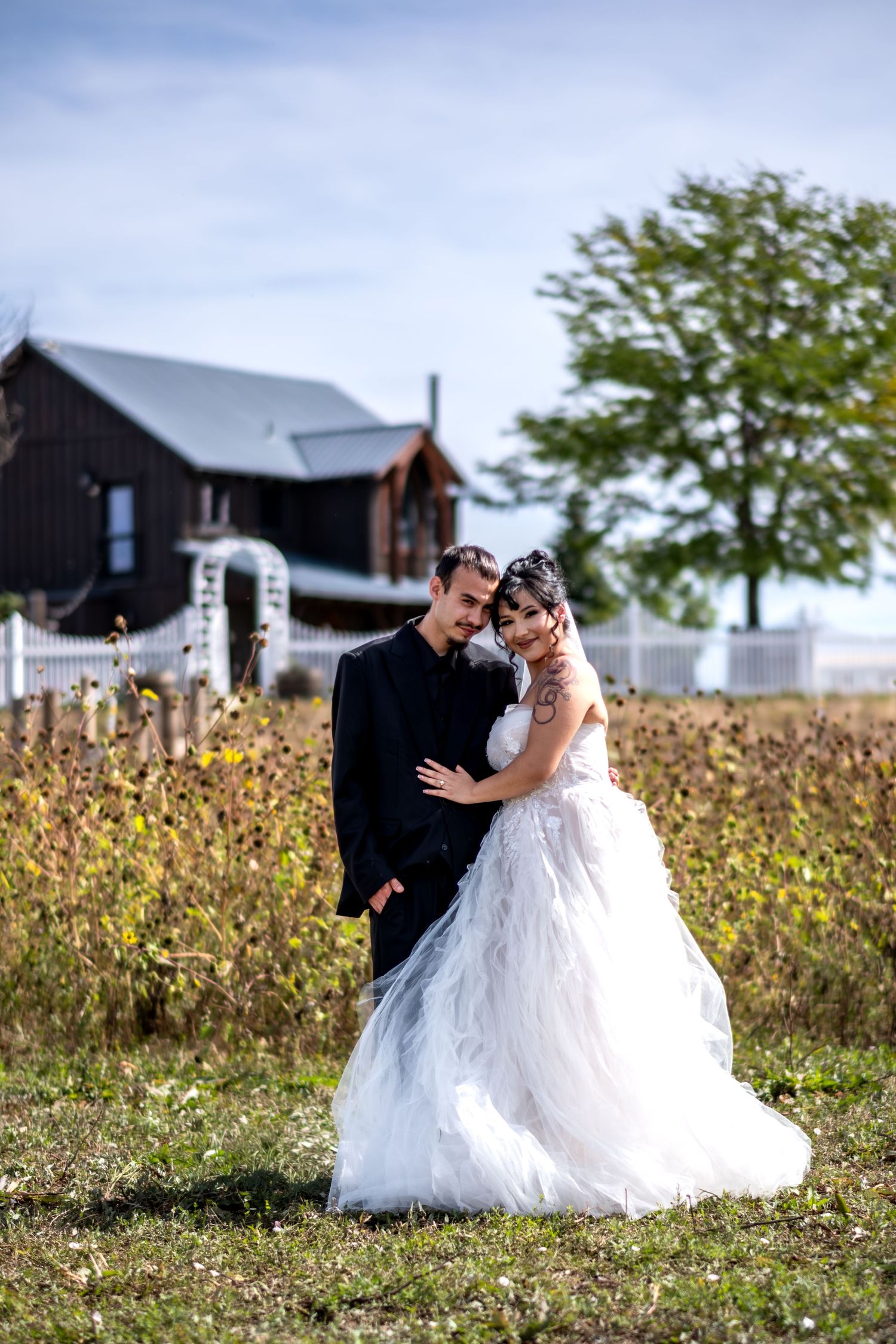 Bride and groom posing in front of a rustic barn, bride wearing a white ballgown wedding dress.