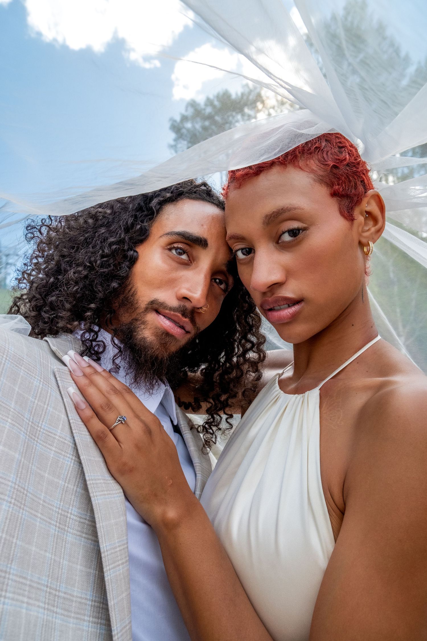 Intimate close-up of interracial wedding couple, bride with short red hair in white halter dress, groom with curly hair.