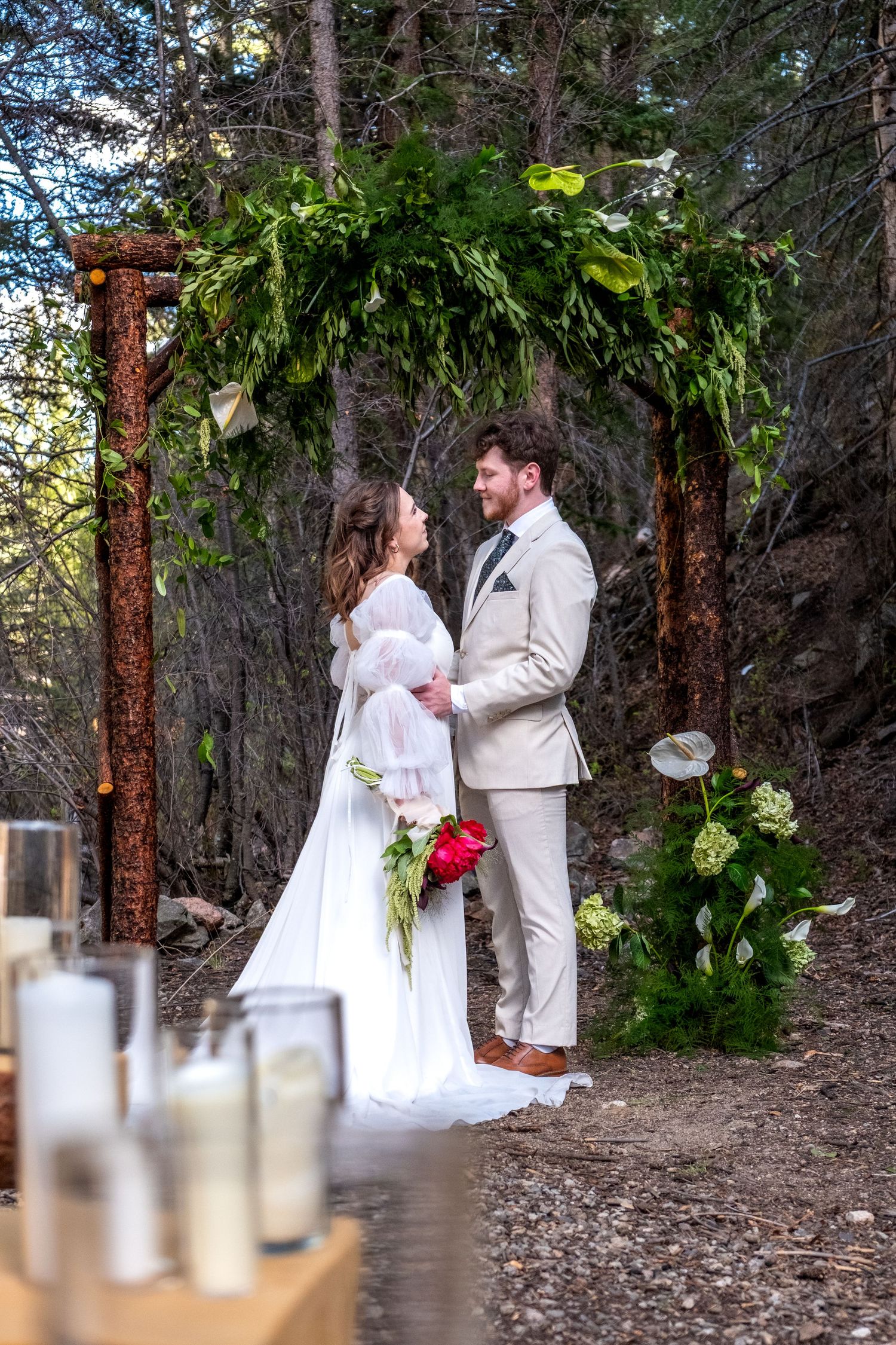Bride and groom exchanging vows under rustic wooden arch adorned with greenery in a forest wedding ceremony.