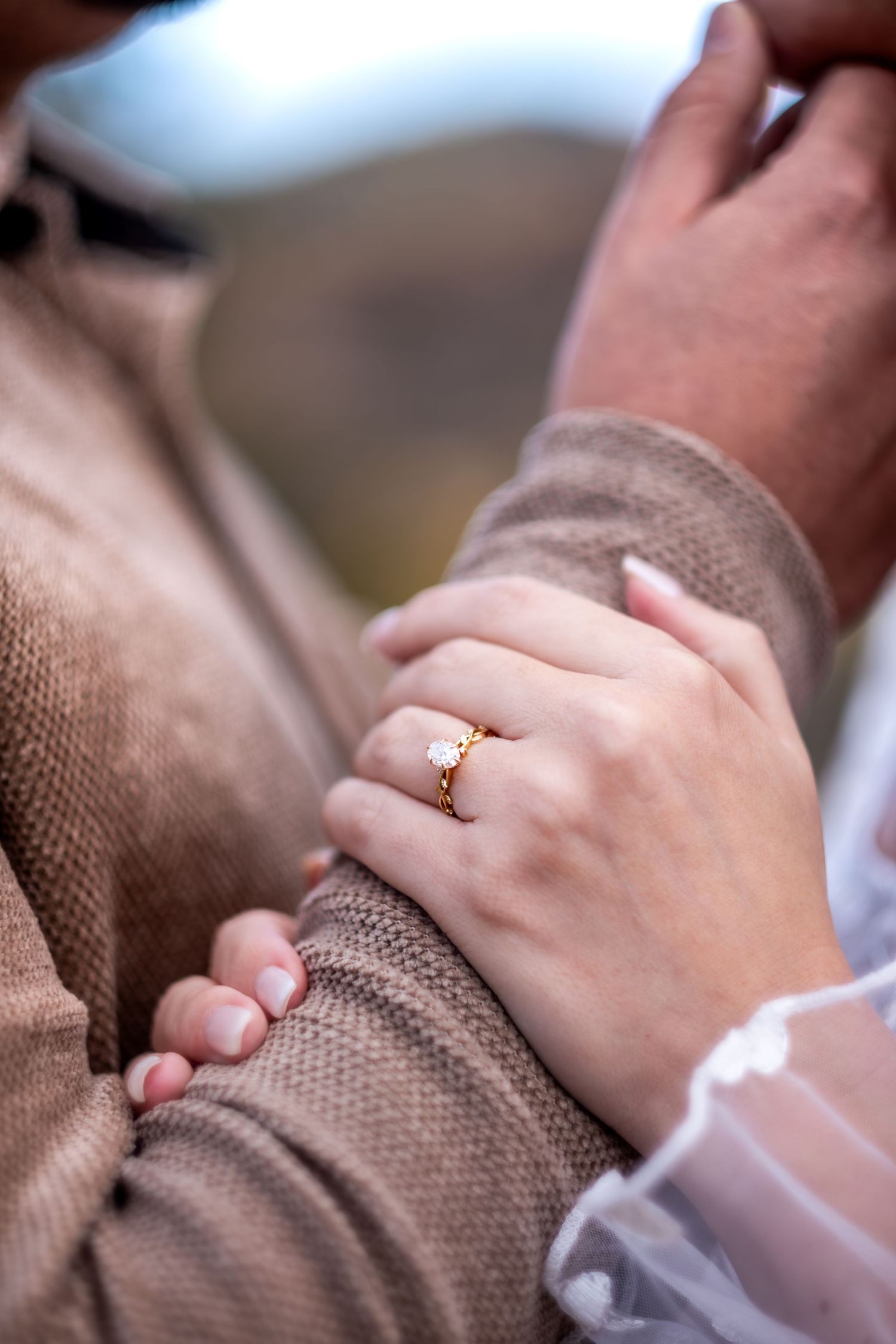 Close-up of a womans hand wearing a gold diamond engagement ring resting on a mans arm.