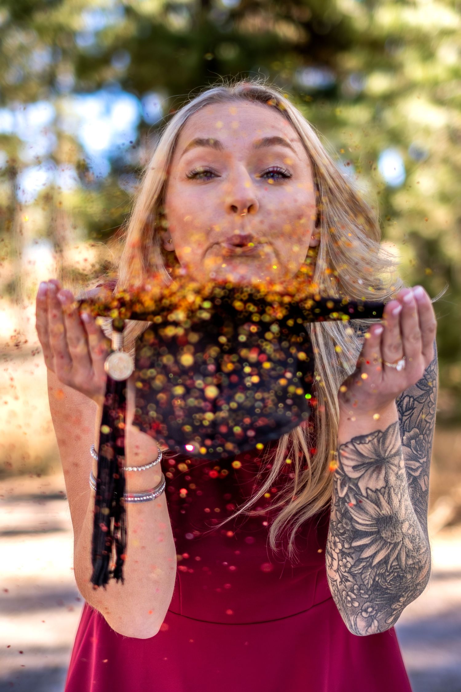 Blonde woman with tattoos blowing gold glitter from her hands outdoors.
