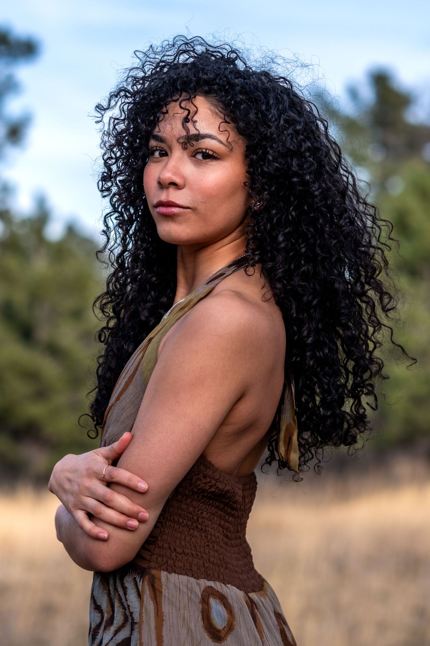Portrait of a woman with long curly black hair in a bohemian dress posing outdoors in golden field.