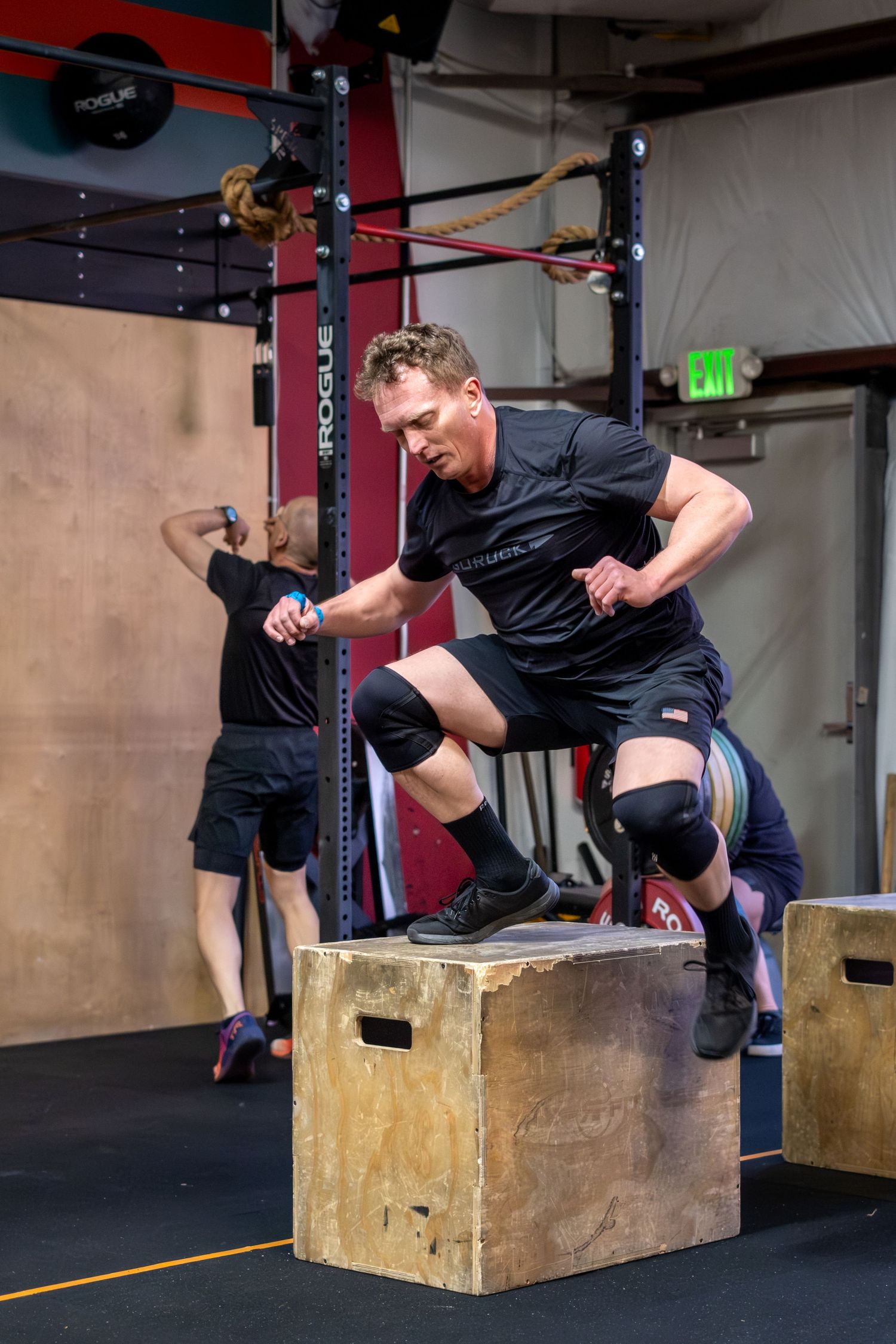 Athletic man jumping onto a wooden plyo box during a CrossFit workout.