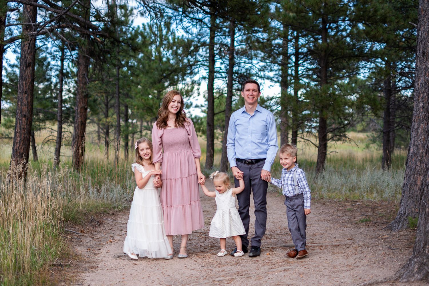 Family of four poses on a forest path, parents with two daughters and a son in coordinated outfits.