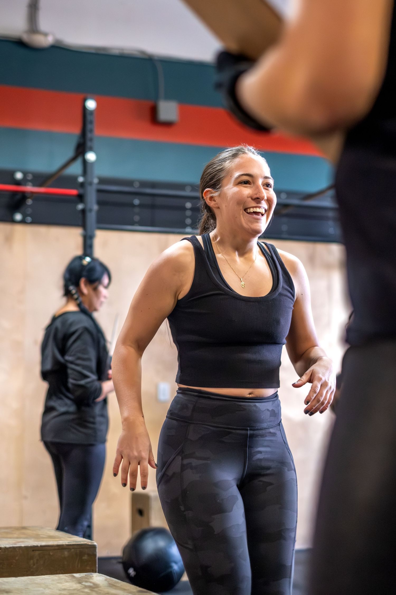 Smiling woman in black workout attire exercising at a CrossFit gym.