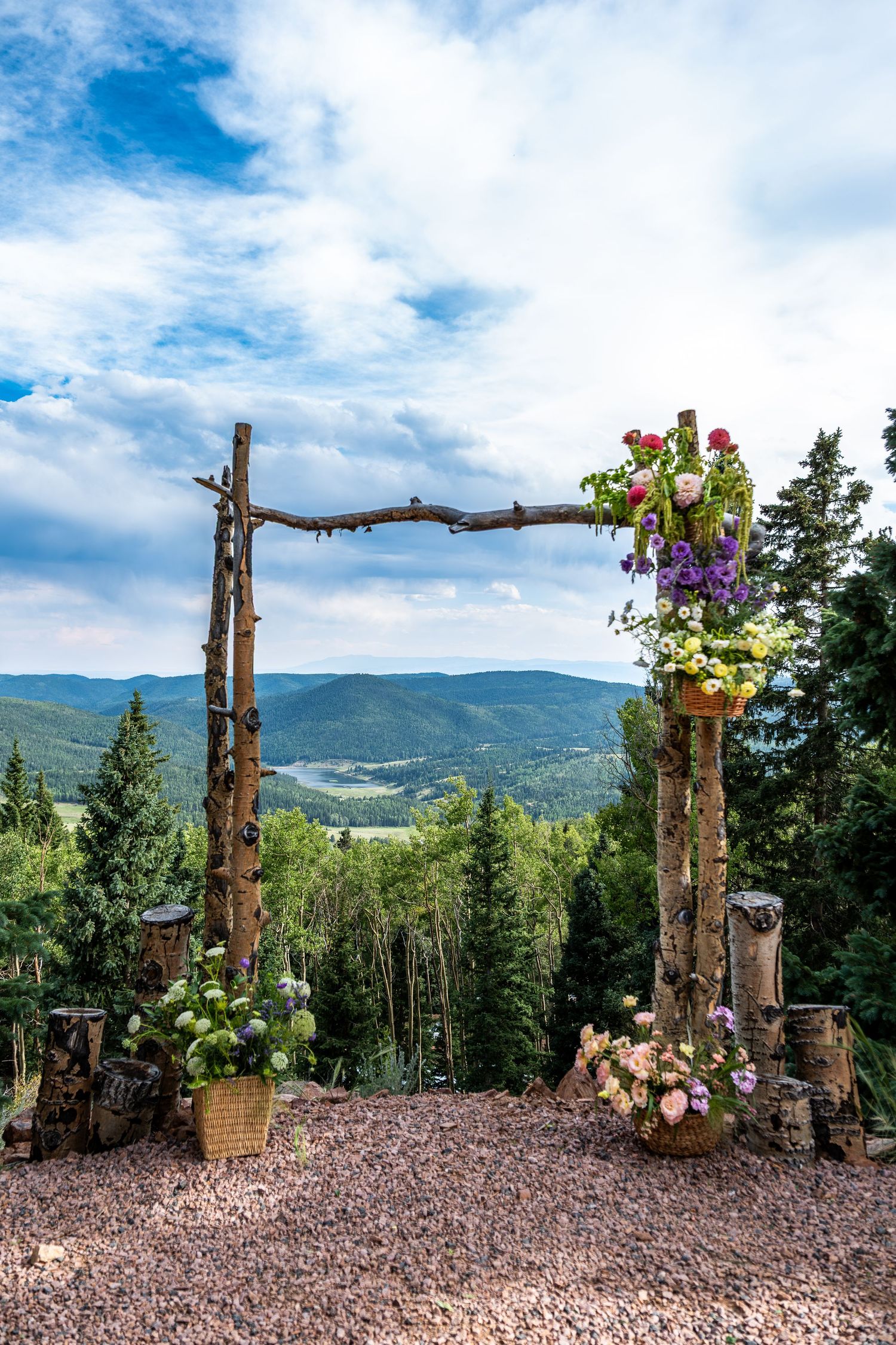 Rustic wooden wedding arch adorned with colorful flowers overlooking lush green mountain landscape.