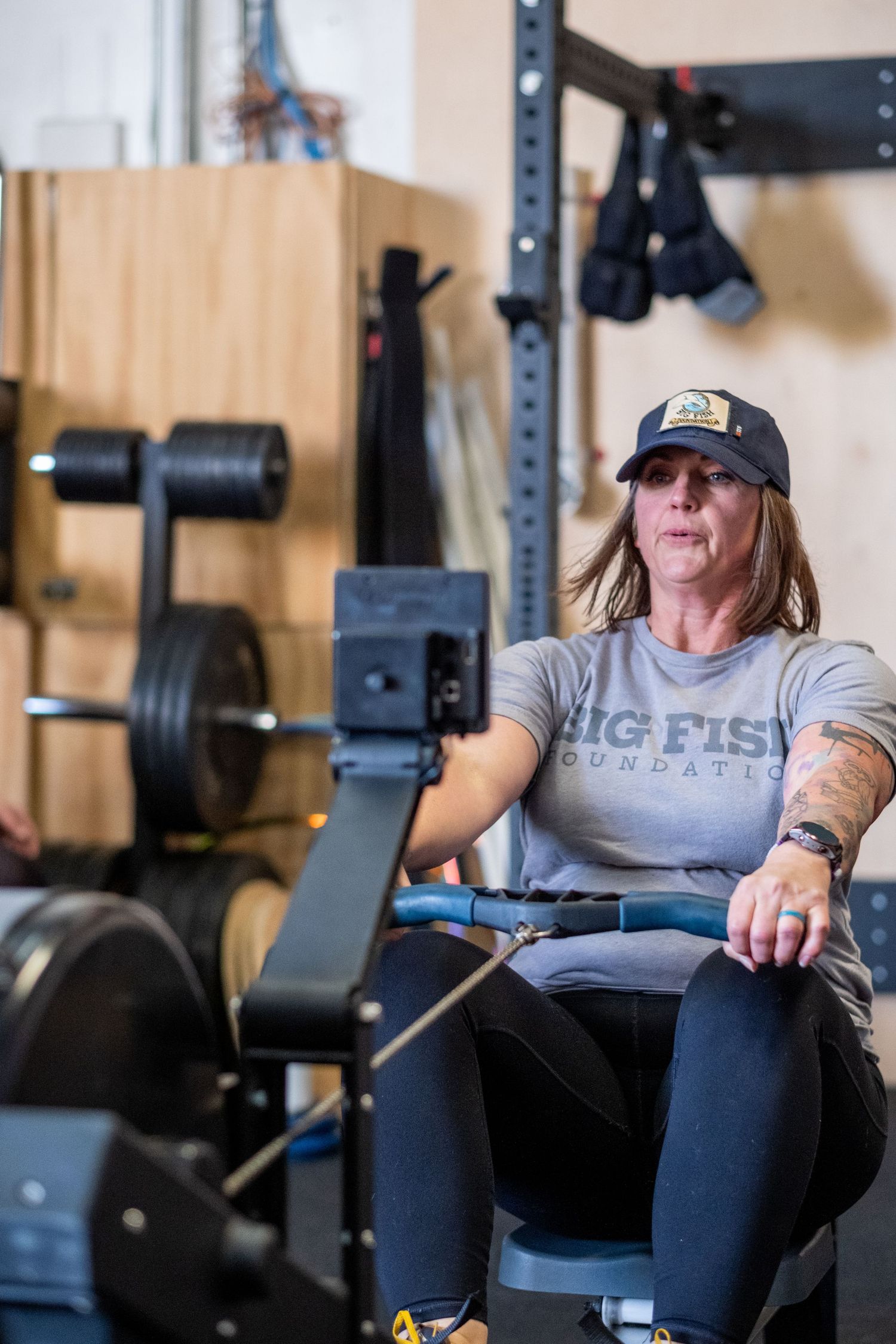 Woman in a Big Fish Foundation shirt rowing on a machine in a CrossFit gym.