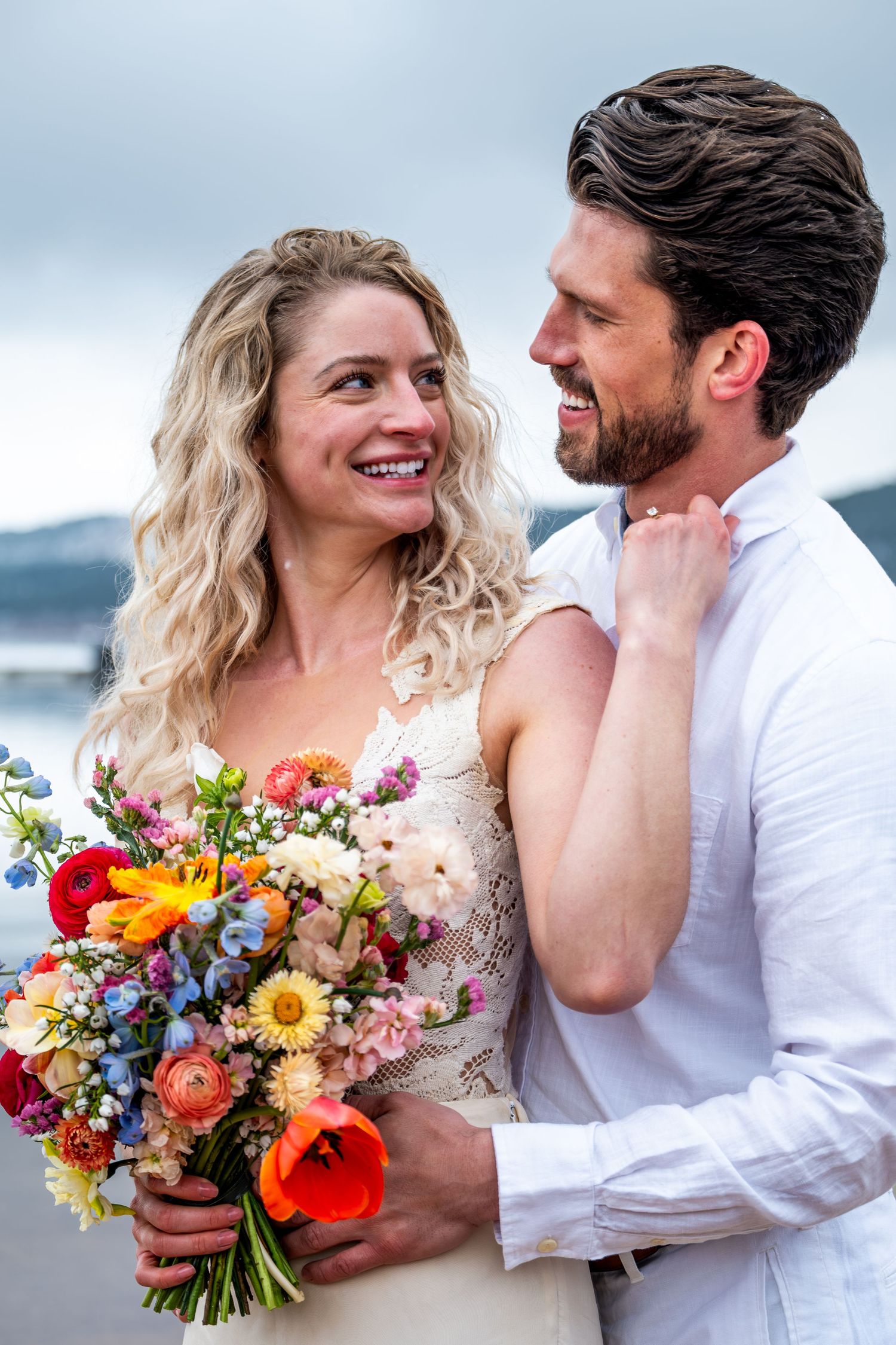 Happy couple at their wedding with bride holding vibrant mixed flower bouquet.