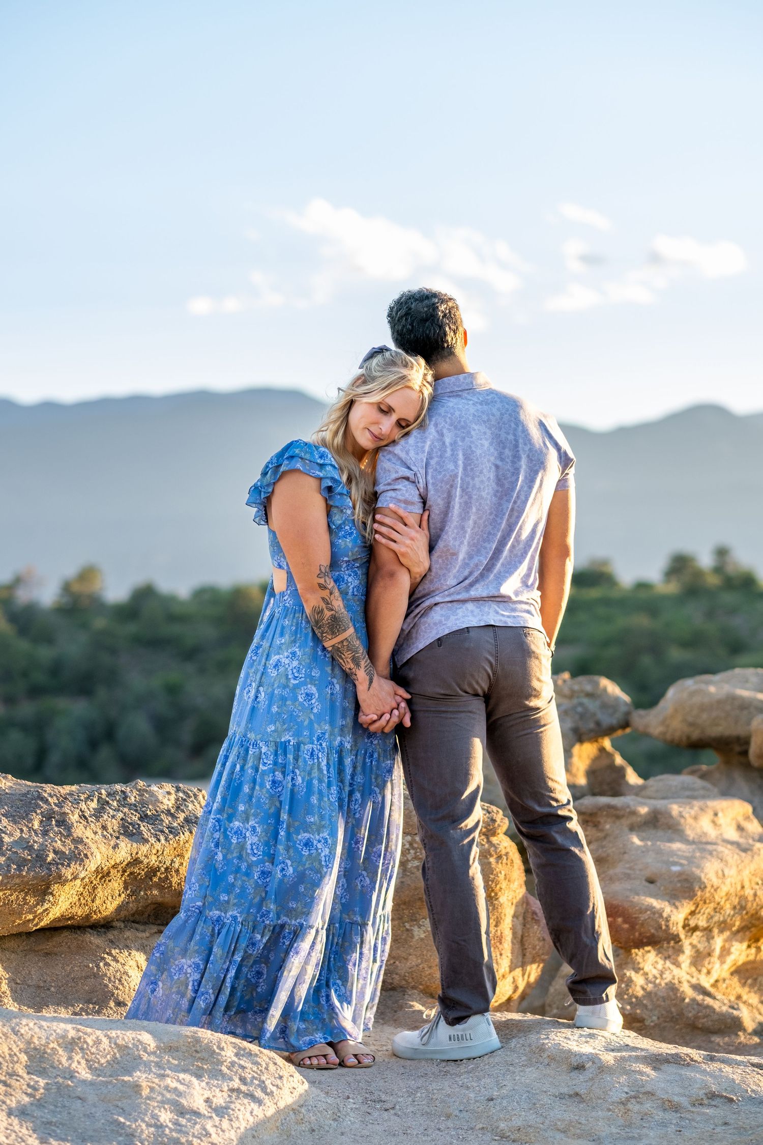 Romantic couple embracing on rocky overlook with stunning mountain landscape at golden hour.