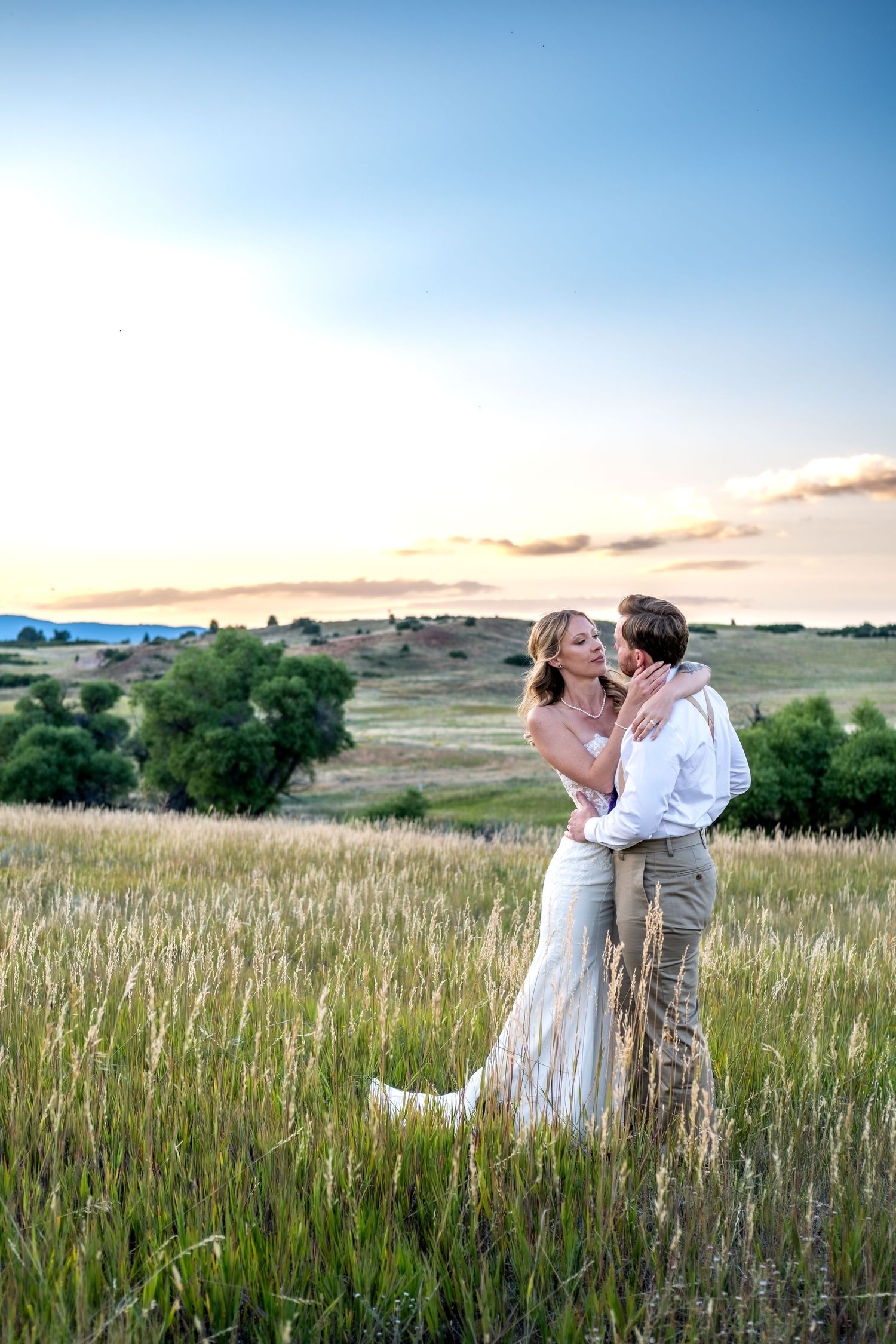 Bride and groom embrace in golden wheat field at sunset, sharing romantic moment in scenic countryside landscape.