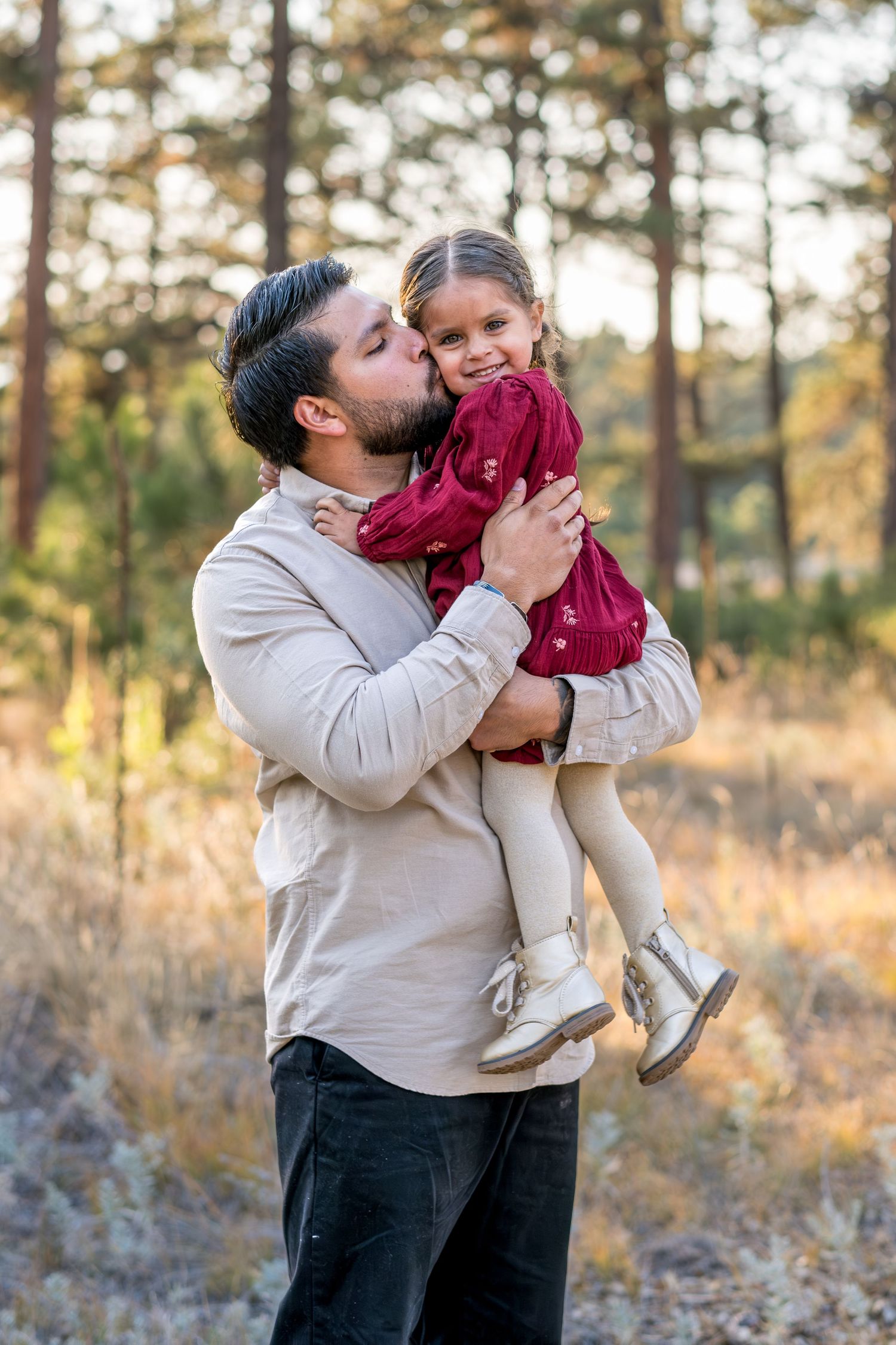 Father kissing his young daughter on the cheek while holding her in an autumn forest.