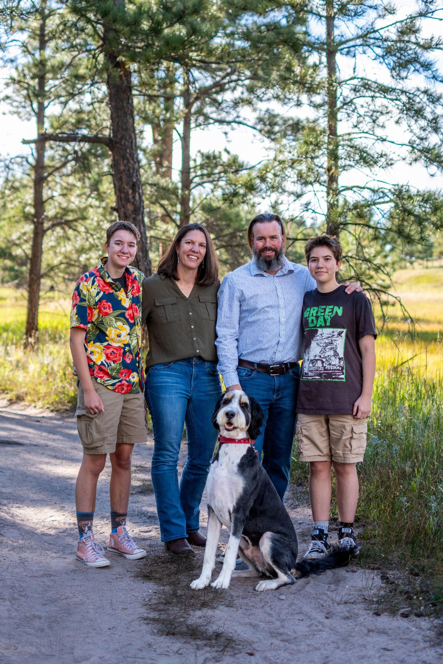 Happy family of four with a Great Dane dog posing on a pine forest trail in summer.