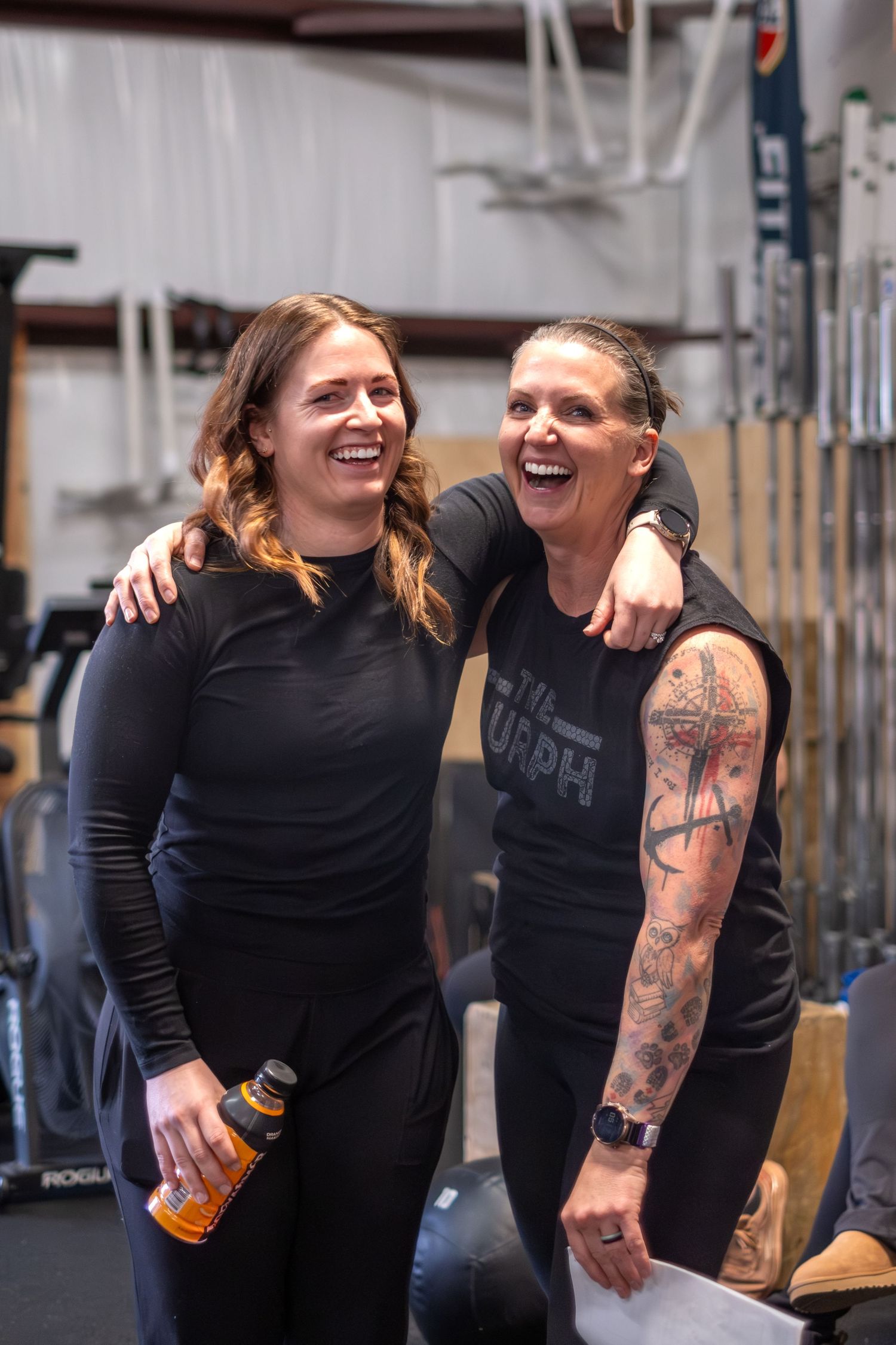 Two women laughing together after a workout in a CrossFit gym setting.