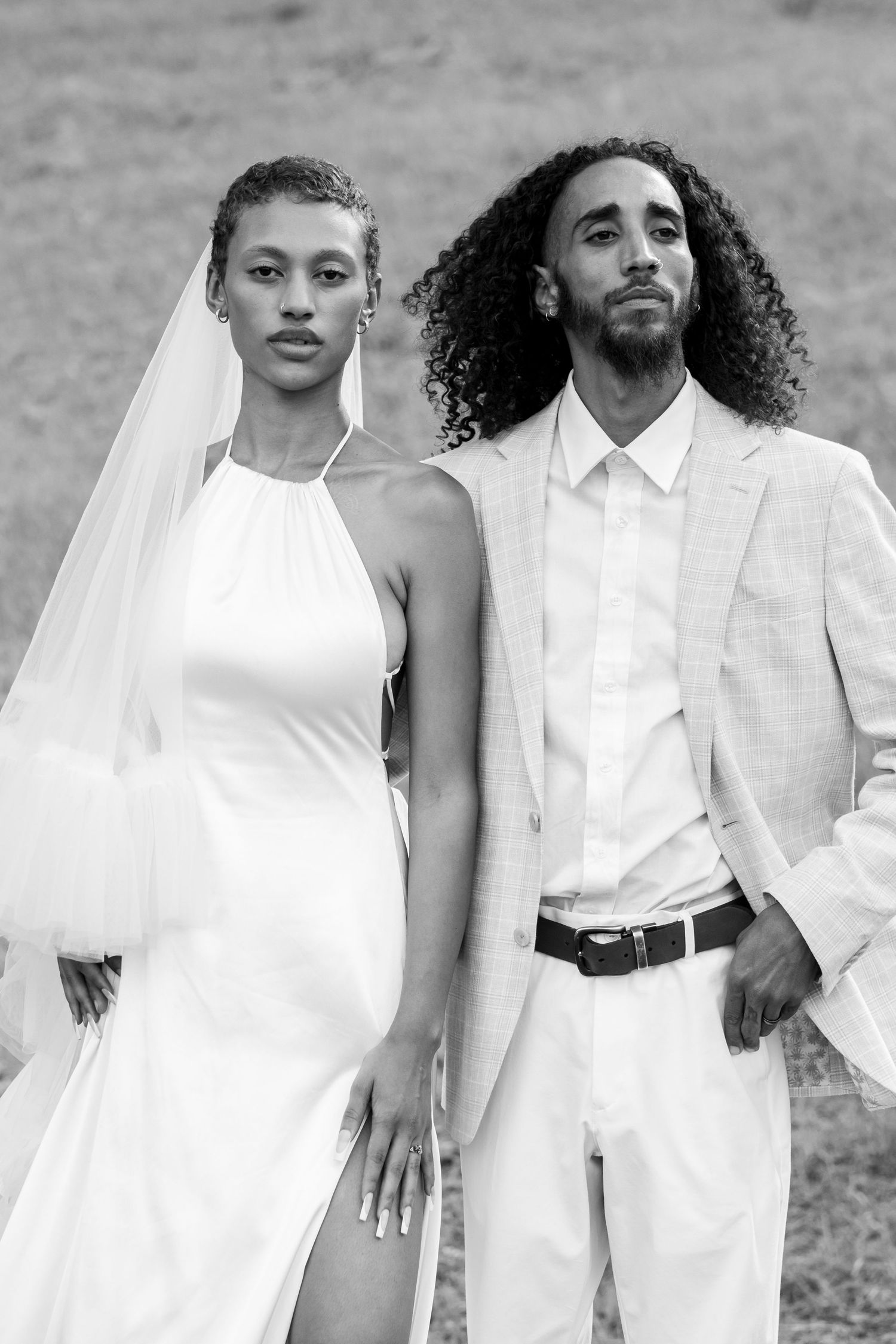 Elegant black and white portrait of bride in halter gown and groom in light suit outdoors.