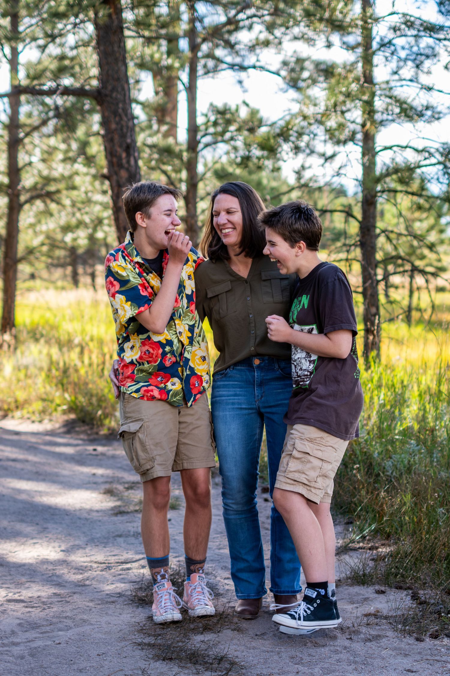 Joyful mother laughing with her two teenage sons on a sunny pine forest trail in summer.