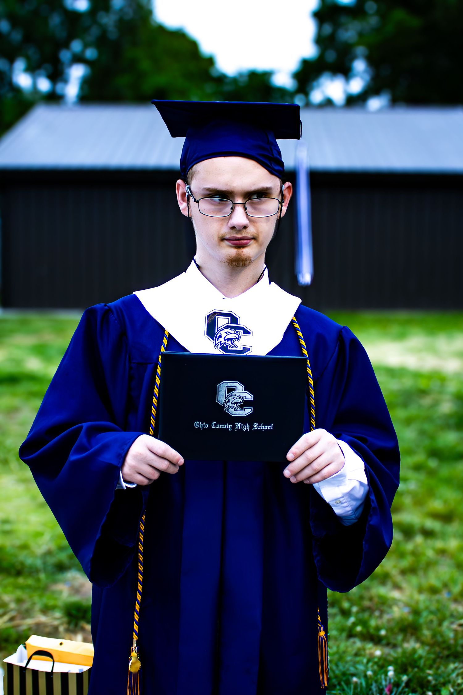 Outdoor senior graduation portrait of a young man in a blue cap and gown taken in Kentucky by Senbon Studio