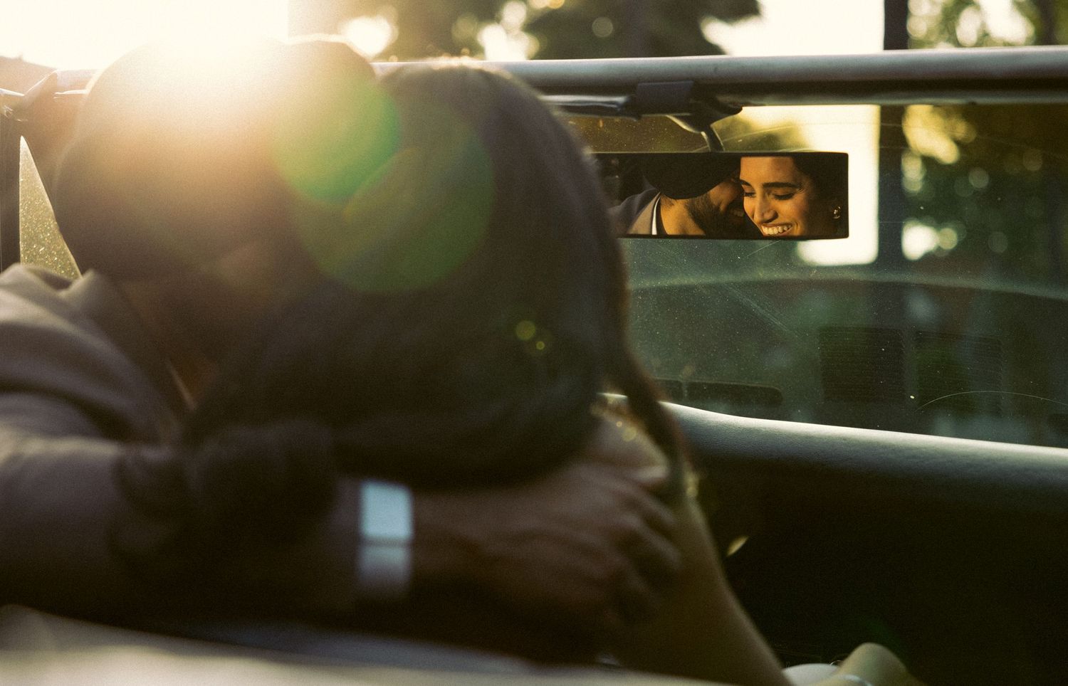 Romantic couple embracing in a car with golden sunlight flaring through the windshield in Beverly Hills.