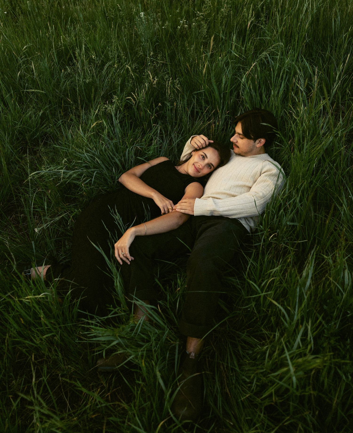 Couple lying together in tall green grass sharing a tender romantic moment outdoors.