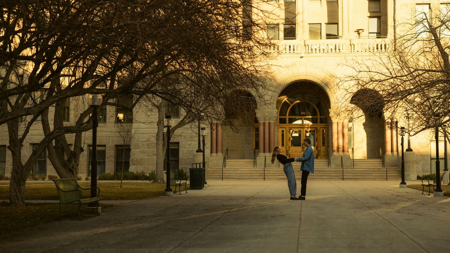 Couple walking hand in hand outside a grand historic building at golden hour.