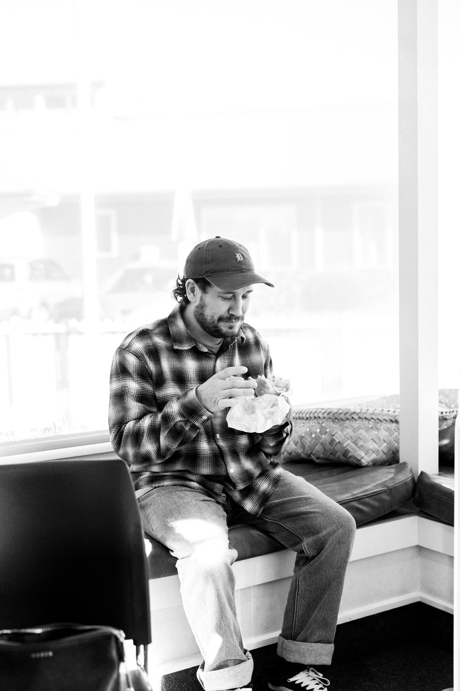 Black and white photo of man sitting by a window holding his newborn baby. Fresh 48 Photography capturing hospital by Nelson Photographer