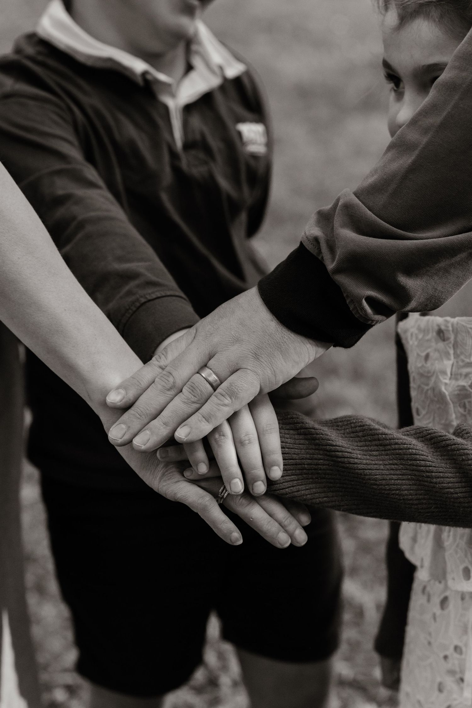 Black and white photo of family hands stacked together, showing unity and connection. Captured by Nelson Family Photographer