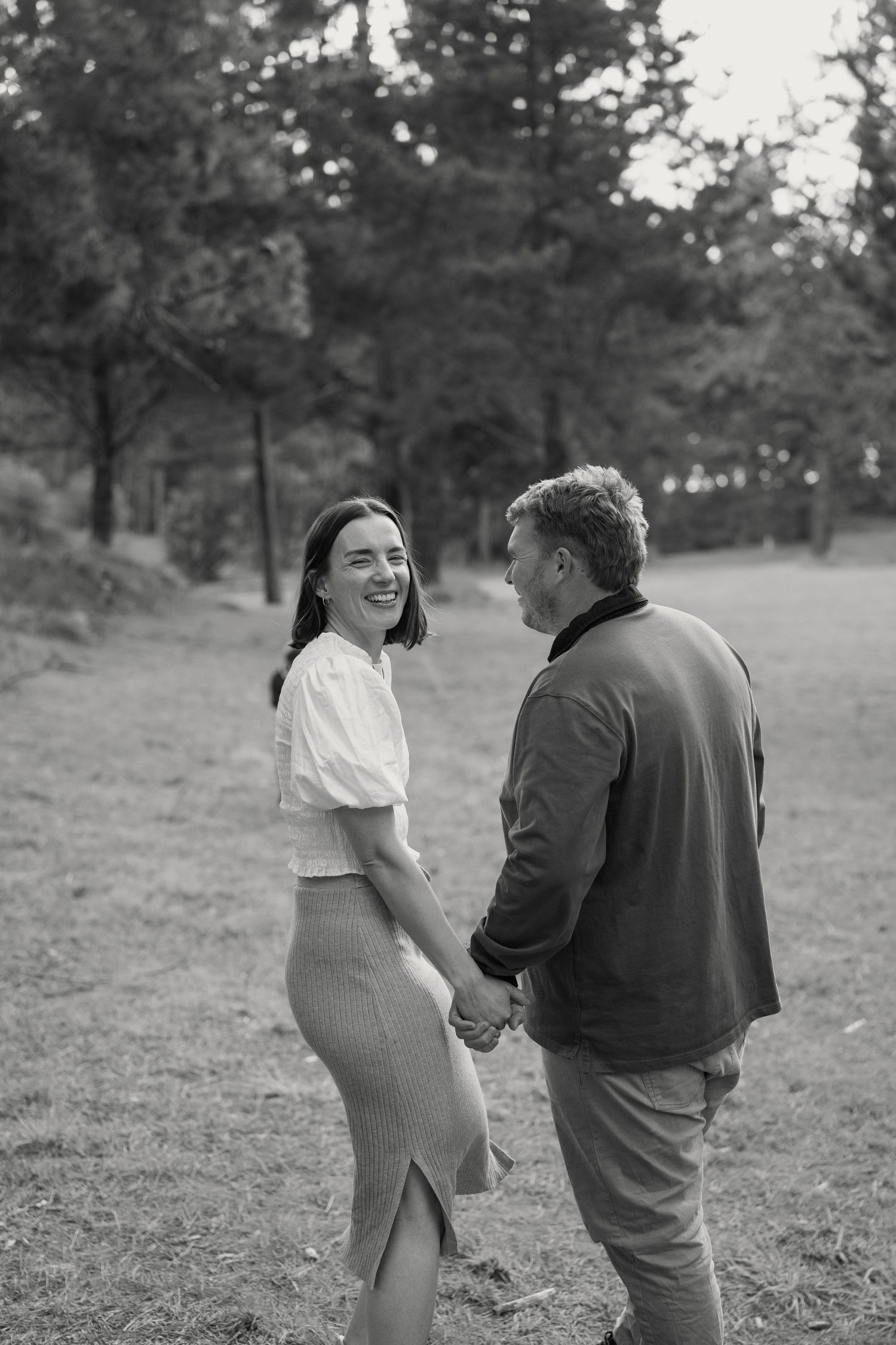 Nelson Family Photography of a smiling couple holding hands in a lush park setting.