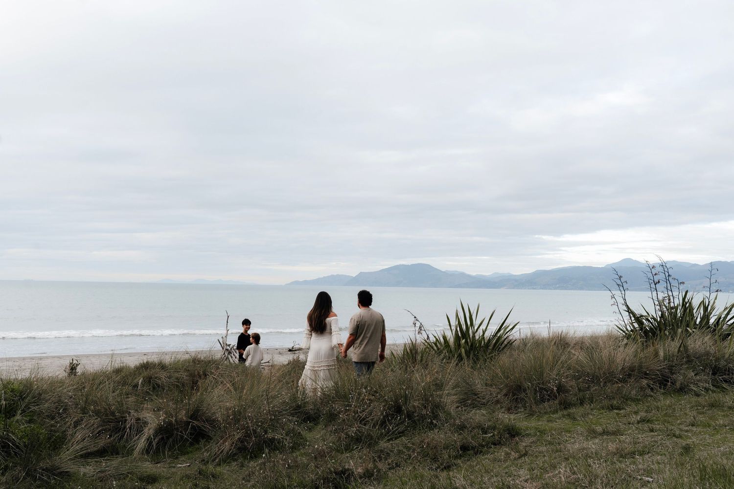 Family standing on a coastal beach with mountains in the background taken by Nelson Family Photographer