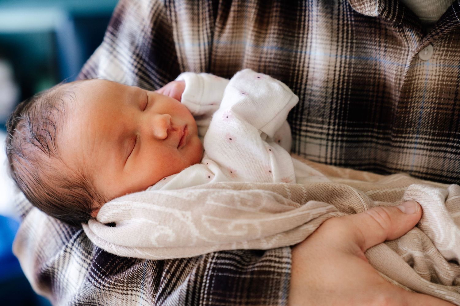 Close-up of a sleeping newborn baby swaddled in a white blanket, held in caring arms. Nelson Newborn Photographer