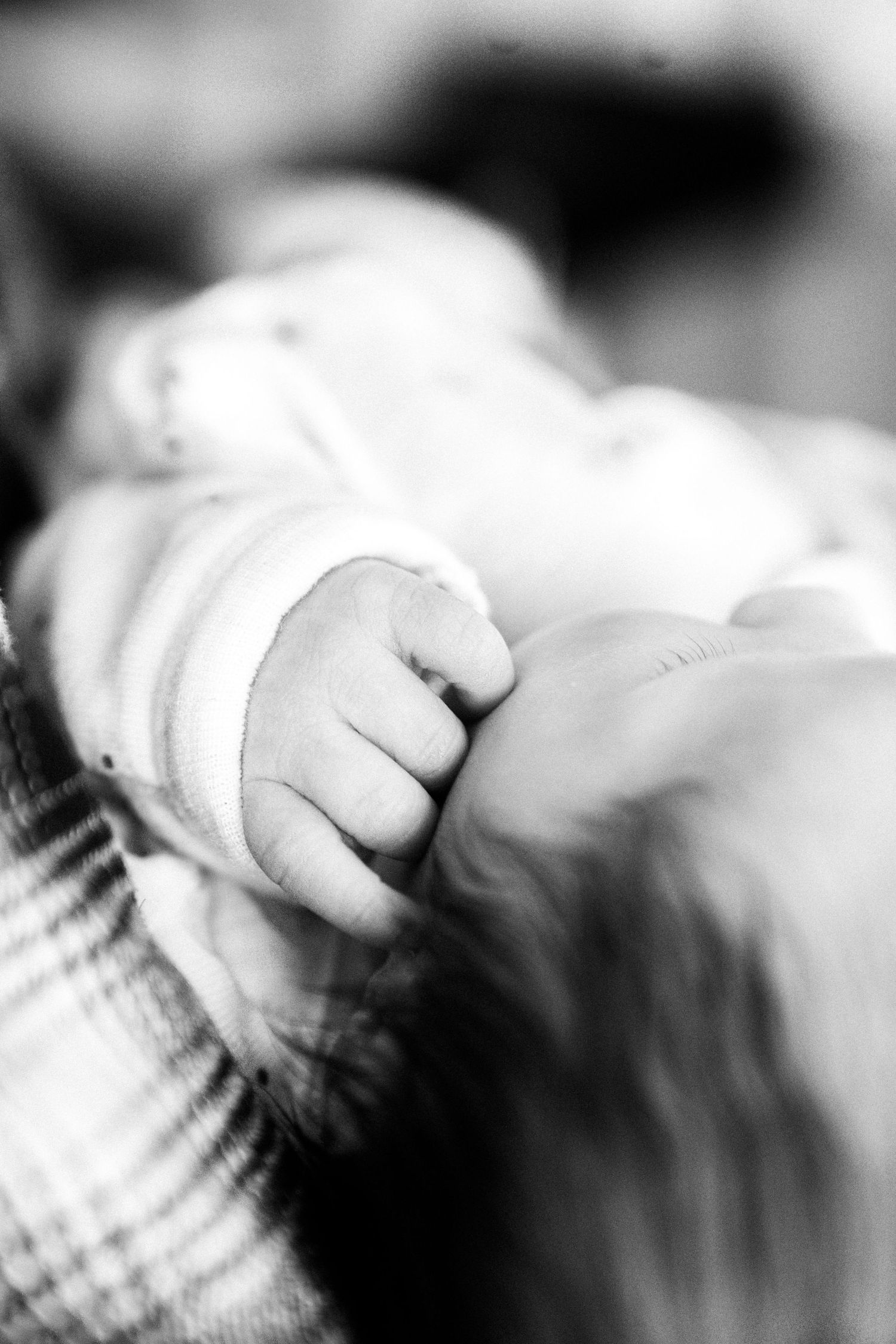 Black and white close-up of a newborn baby's tiny clenched fist in soft focus. Nelson newborn photography