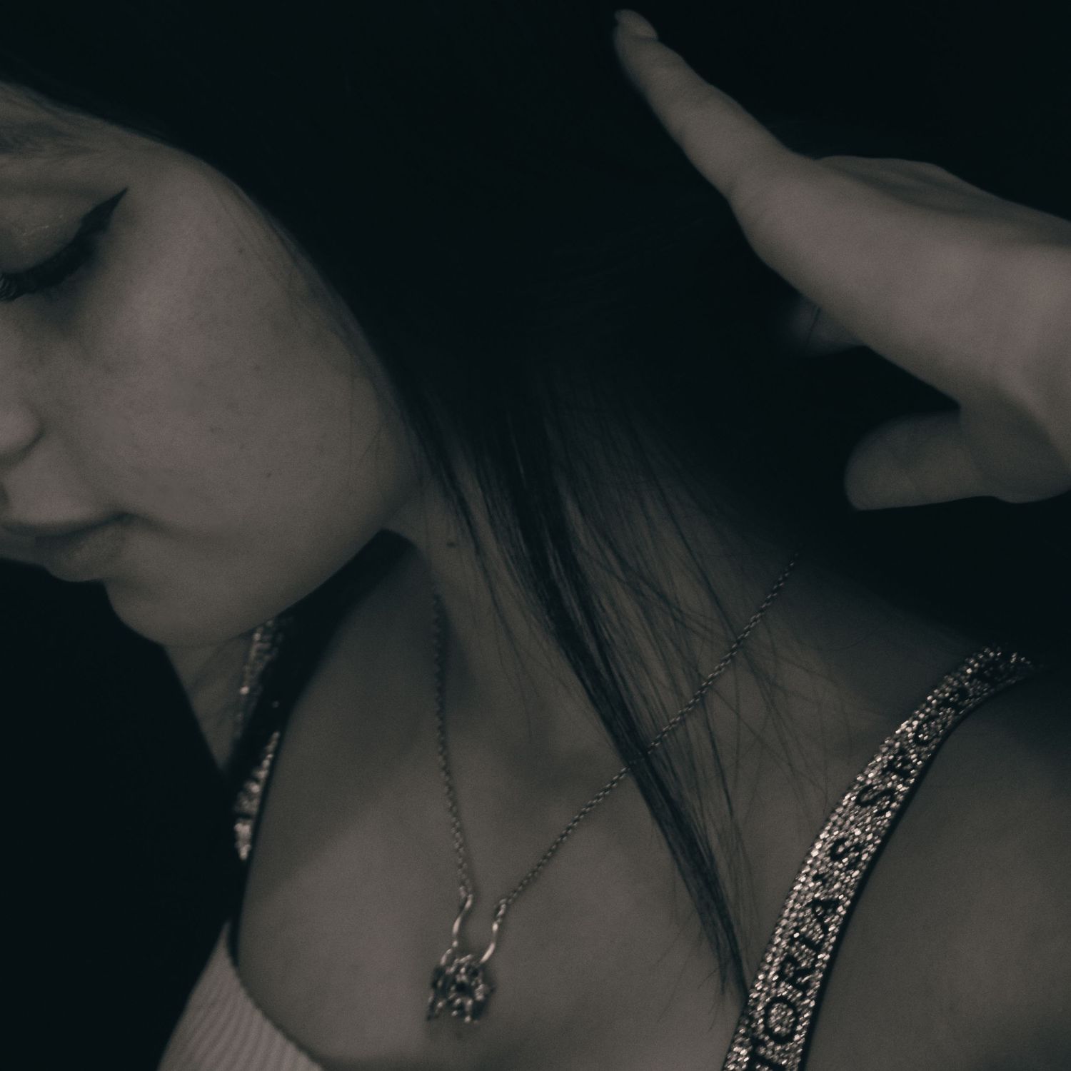 Moody black and white portrait of a young woman with a necklace, looking down in dramatic low-key lighting.