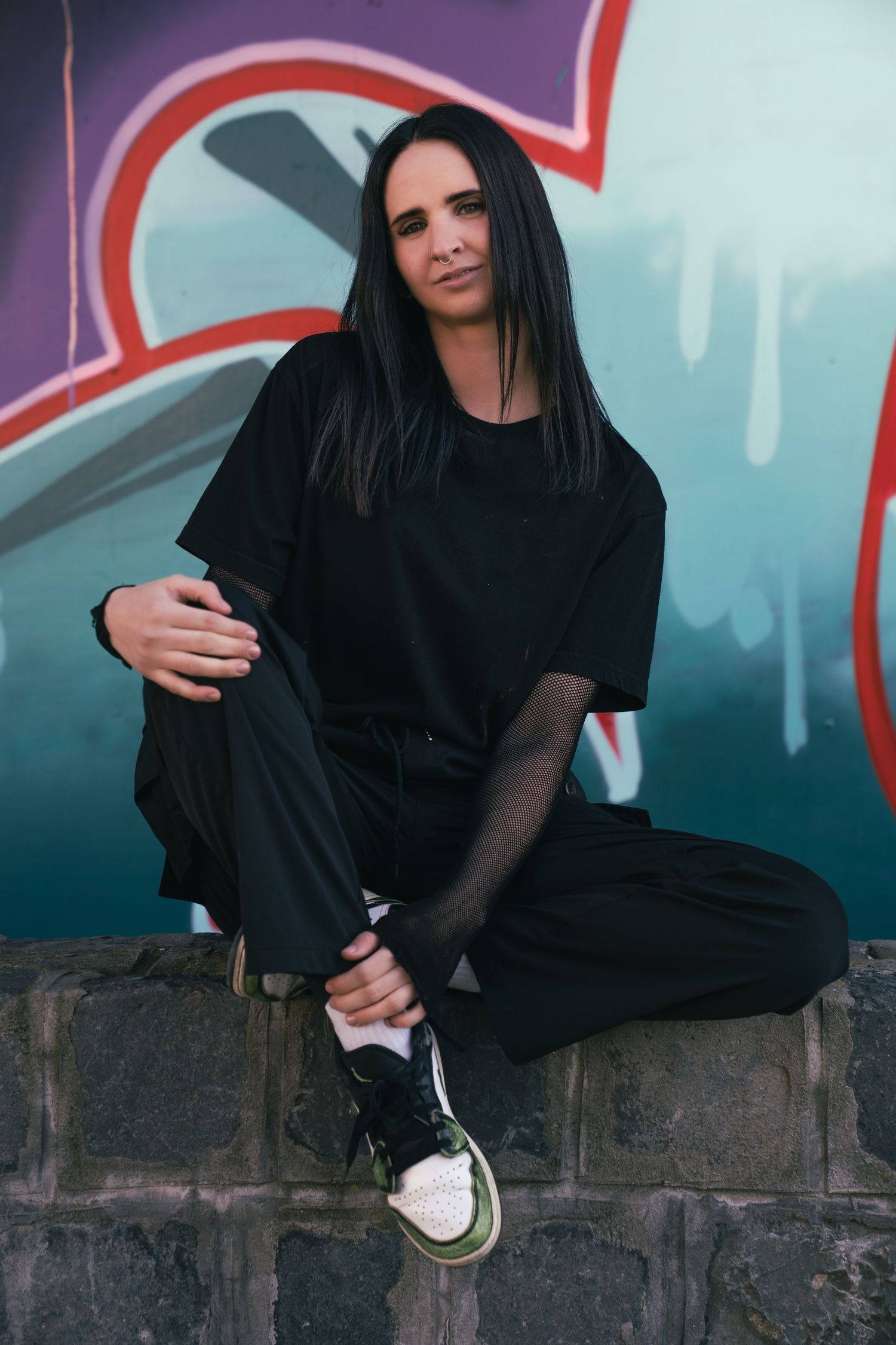 Bencze Máté fotós által készített fotó a egy nőről aki a graffiti előtt ül.