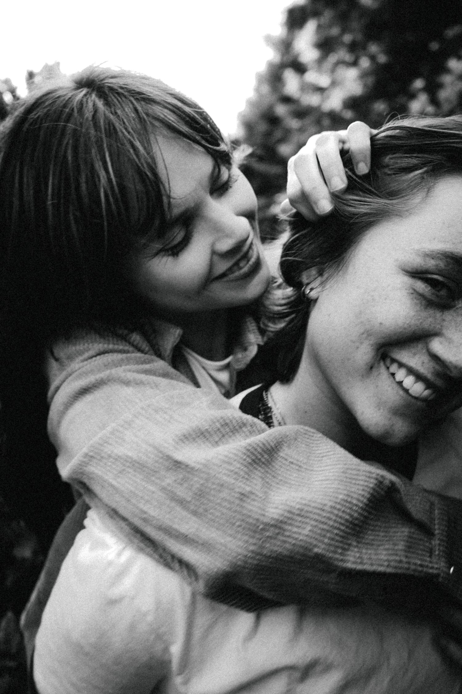 Black and white photo of two people laughing outdoors, one playfully touching the others hair.