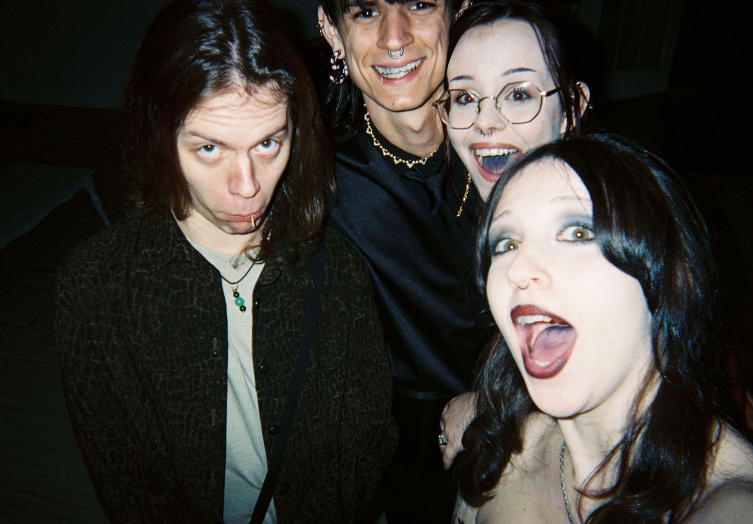 Four young people making fun silly faces together at an indoor gothic-themed celebration.