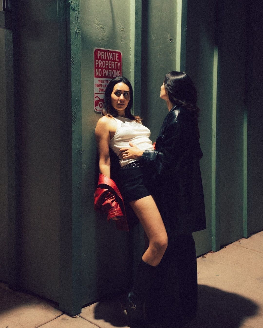 Two women sharing an intimate moment leaning against a wall on a city street at night.
