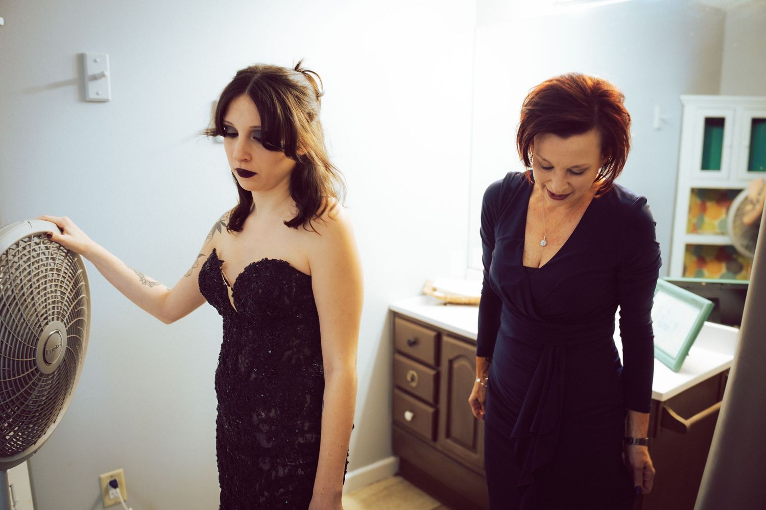 Bride in black strapless lace gown being helped by woman in black dress in preparation room.