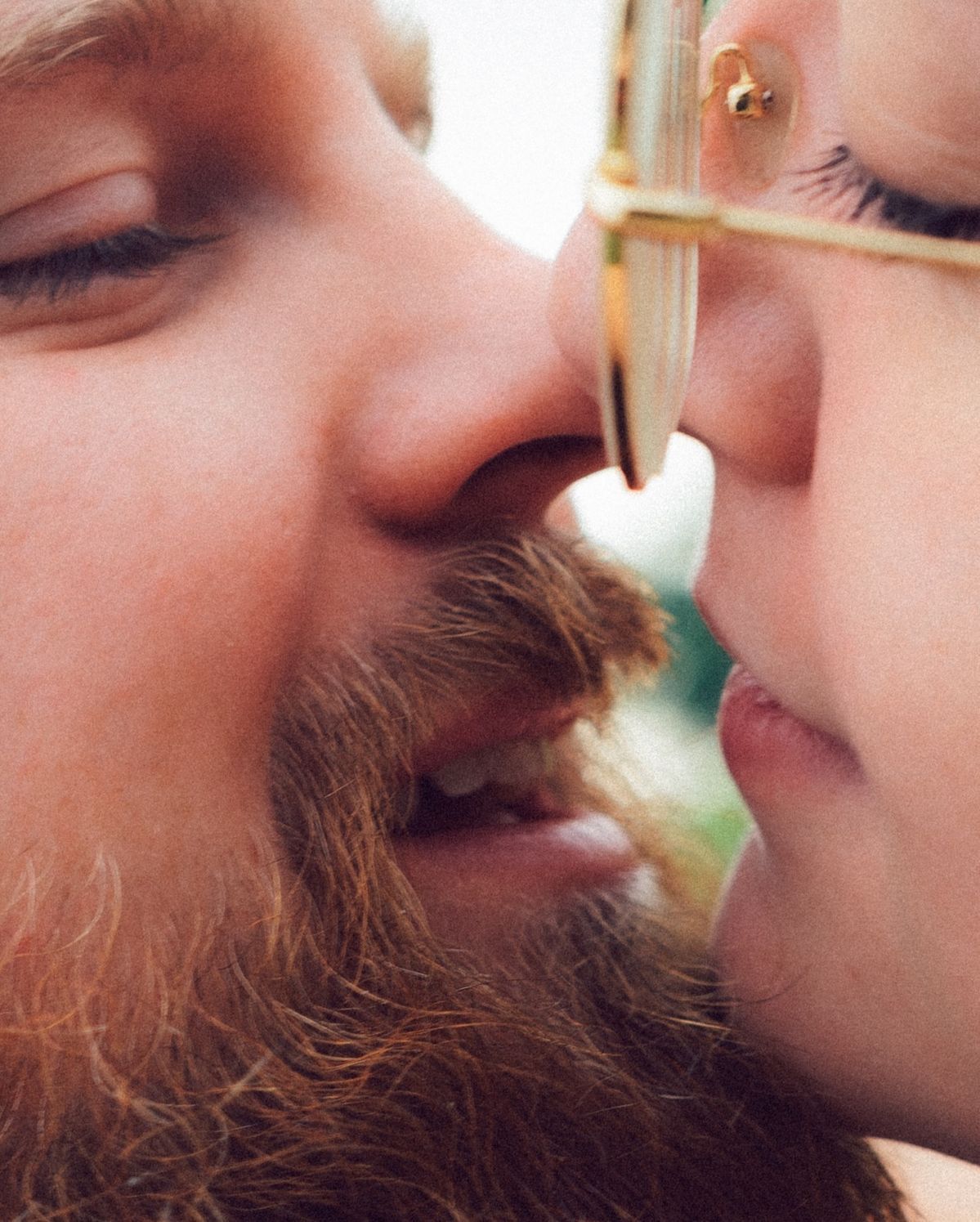 Close-up of bearded man and woman sharing a kiss, man wearing gold-framed glasses.