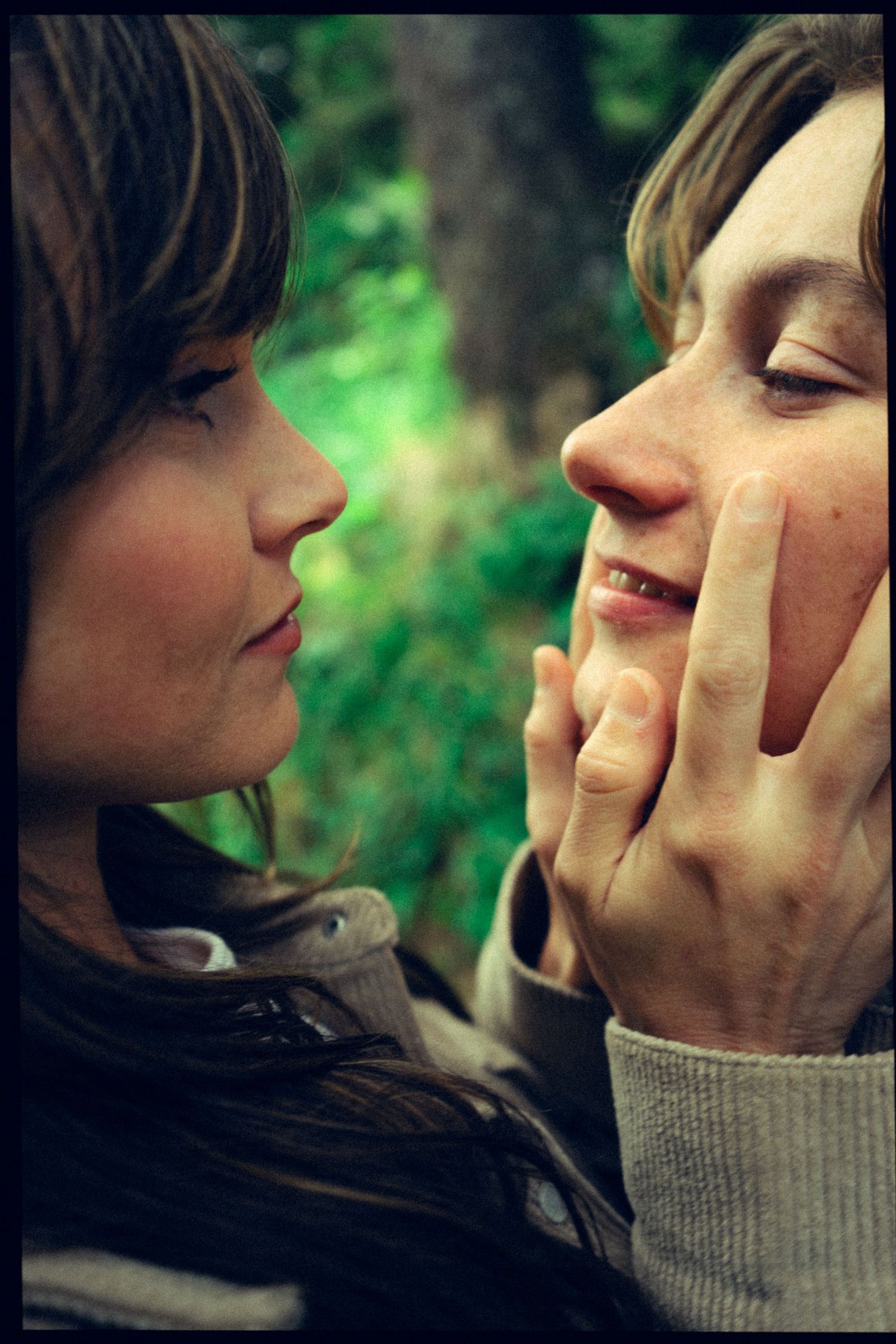 Two women sharing an intimate moment outdoors with one gently touching the others face.