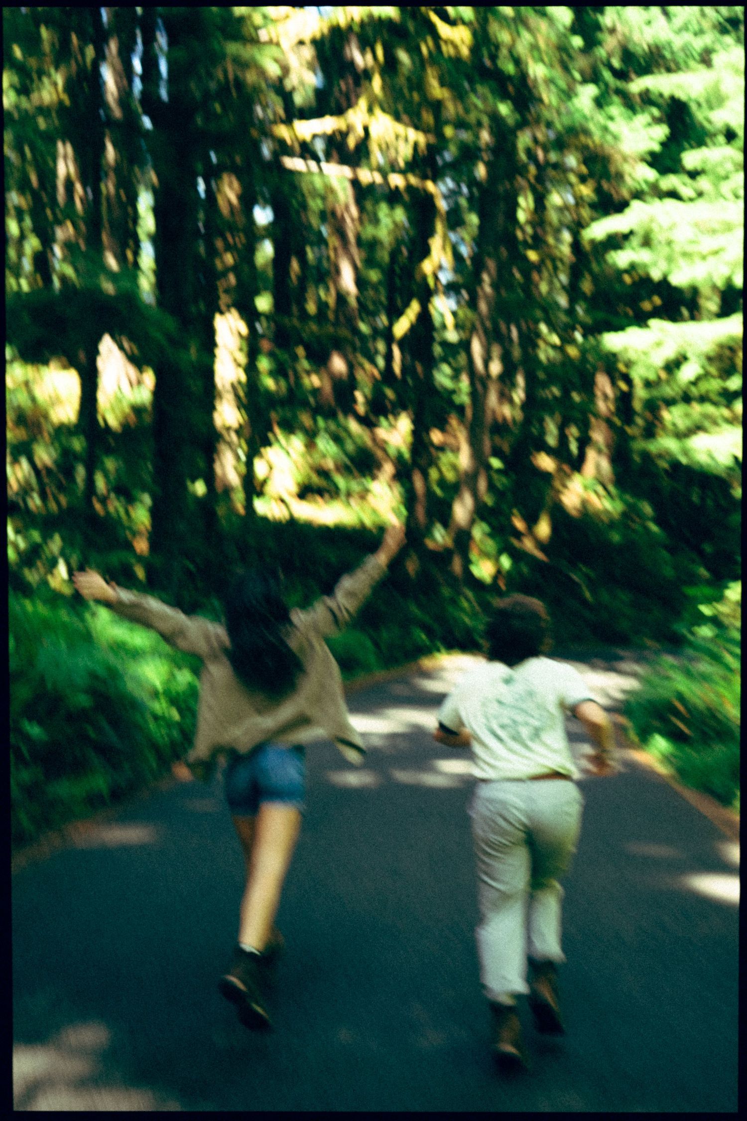 Two people running together down a forest road surrounded by tall green trees in a blurred motion photo.