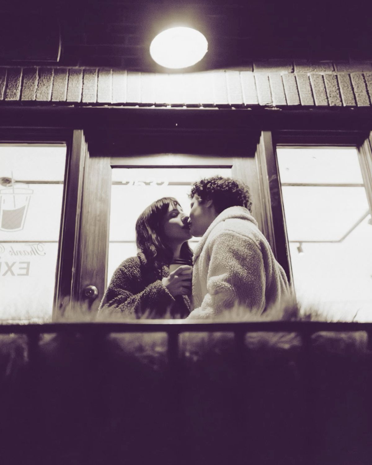 Romantic couple sharing a kiss in a doorway illuminated by warm light at night.